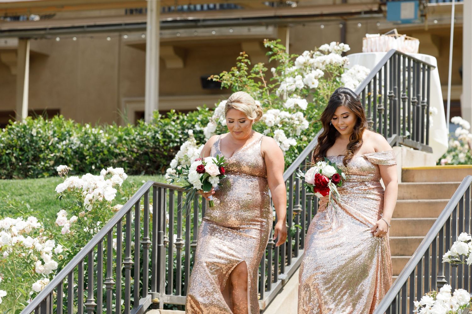 A group in elegant champagne-colored bridesmaid dresses poses together on outdoor stairs at a wedding venue.
