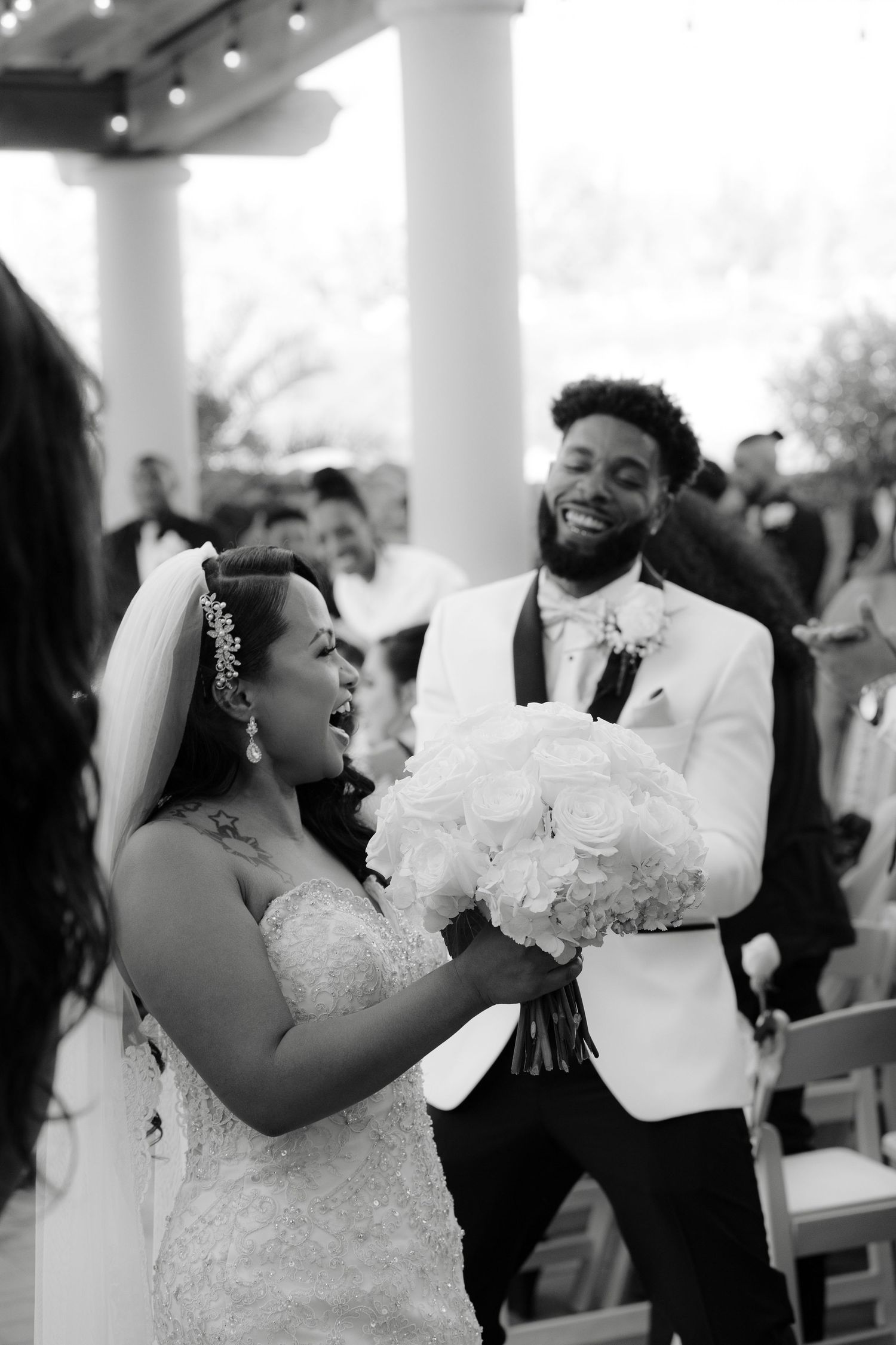 A joyful couple shares a candid moment of laughter during their wedding celebration under a columned venue.
