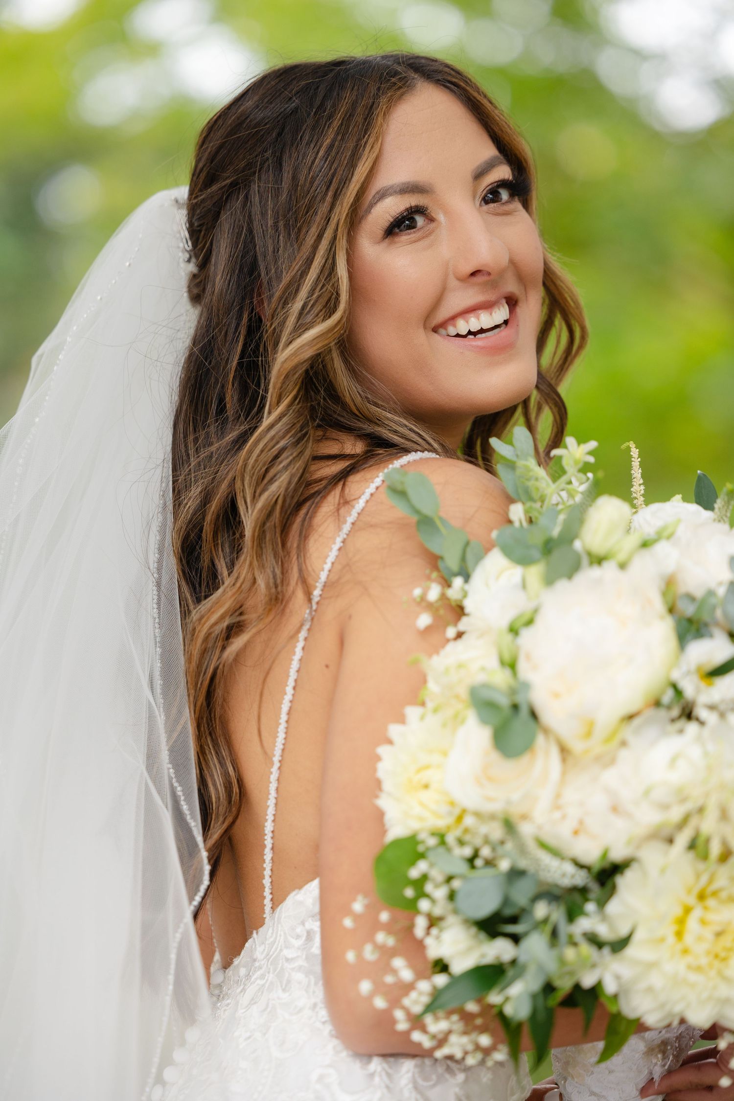 A radiant bride in a white wedding dress holds a beautiful bouquet of cream roses and greenery on her special day.