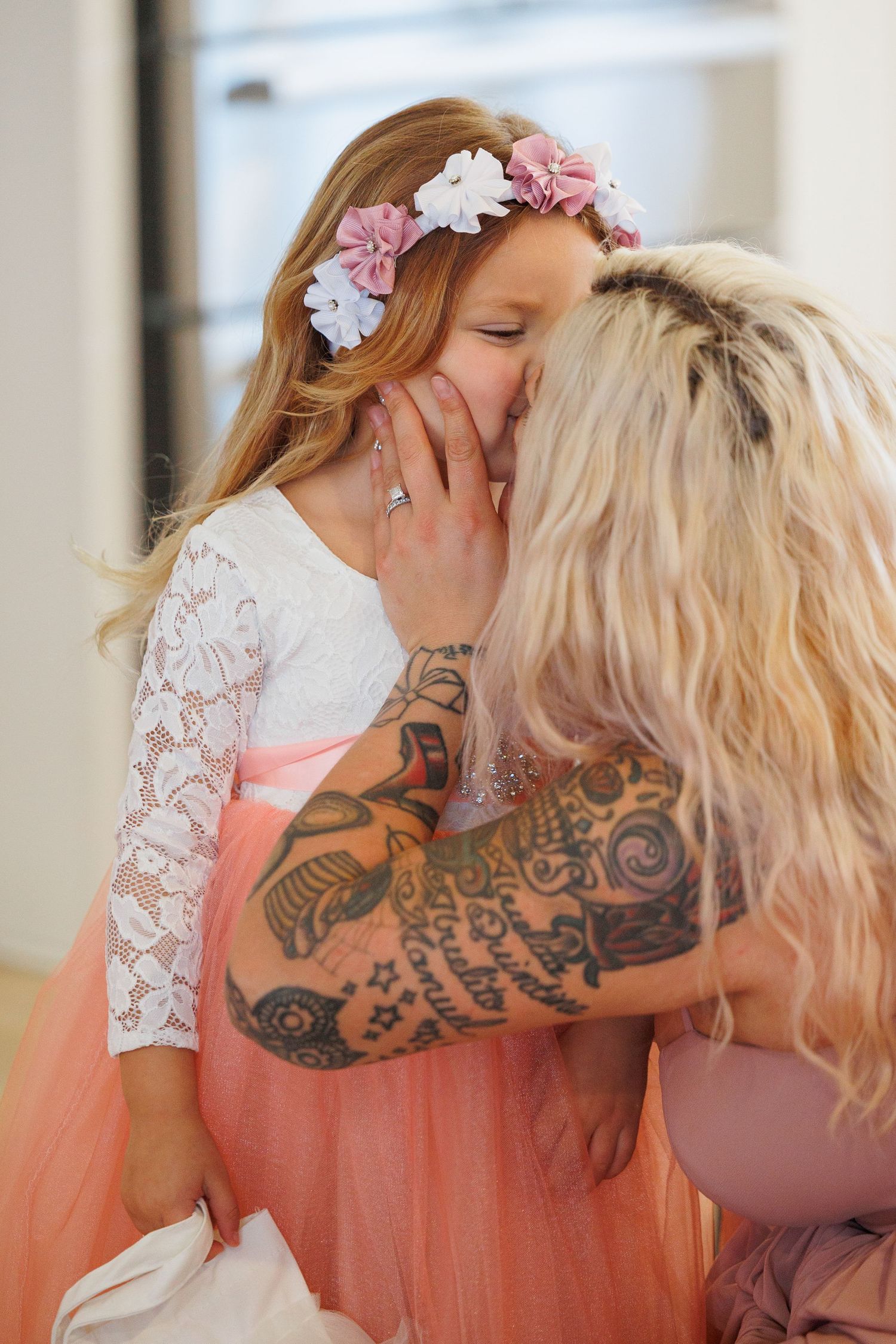 Two people in formal attire share an intimate moment, with visible tattoo art and delicate lace details.