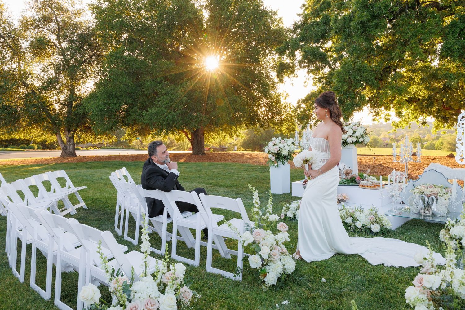 White folding chairs arranged on a grassy lawn for an outdoor wedding ceremony at sunset with golden sunlight.