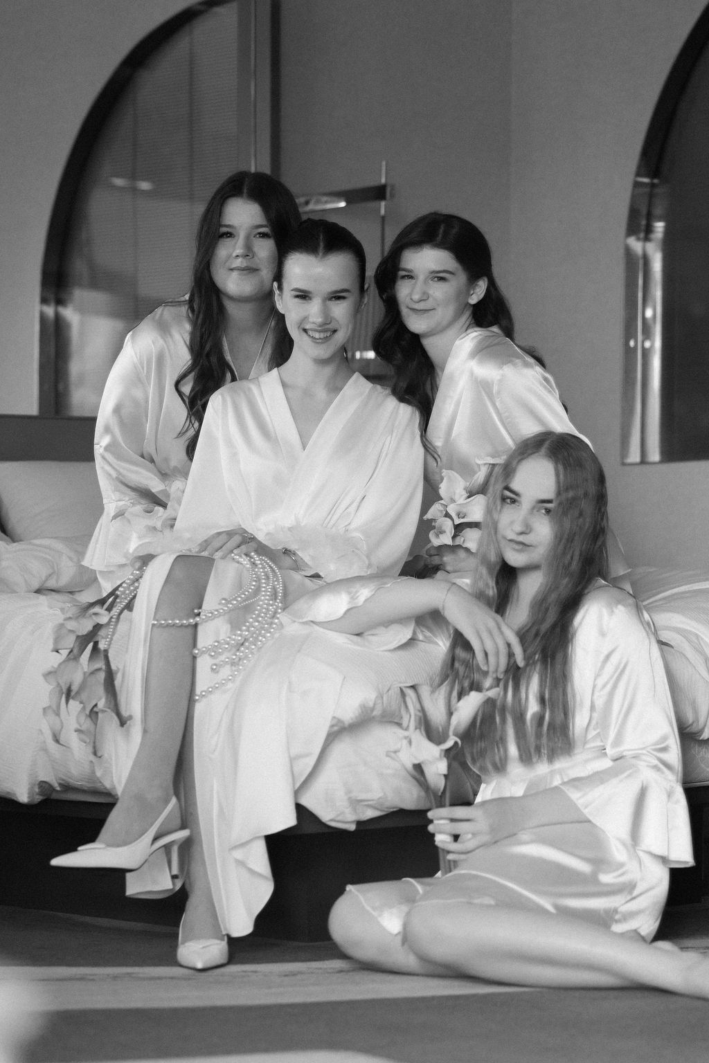 Group wearing white silk robes relaxing together during wedding preparation photoshoot.