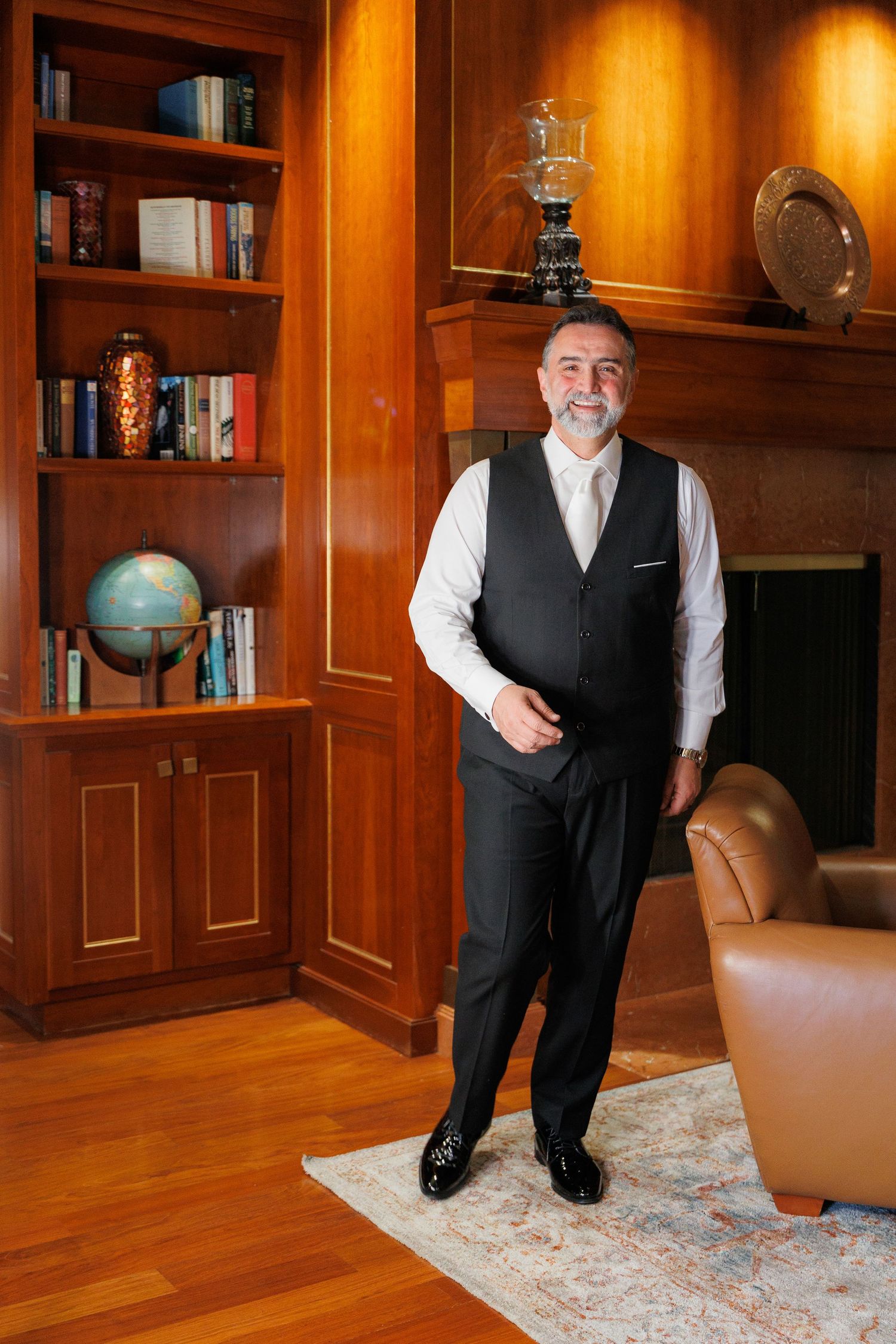 Person in business attire standing in elegant wood-paneled library with built-in bookshelves and oriental rug.