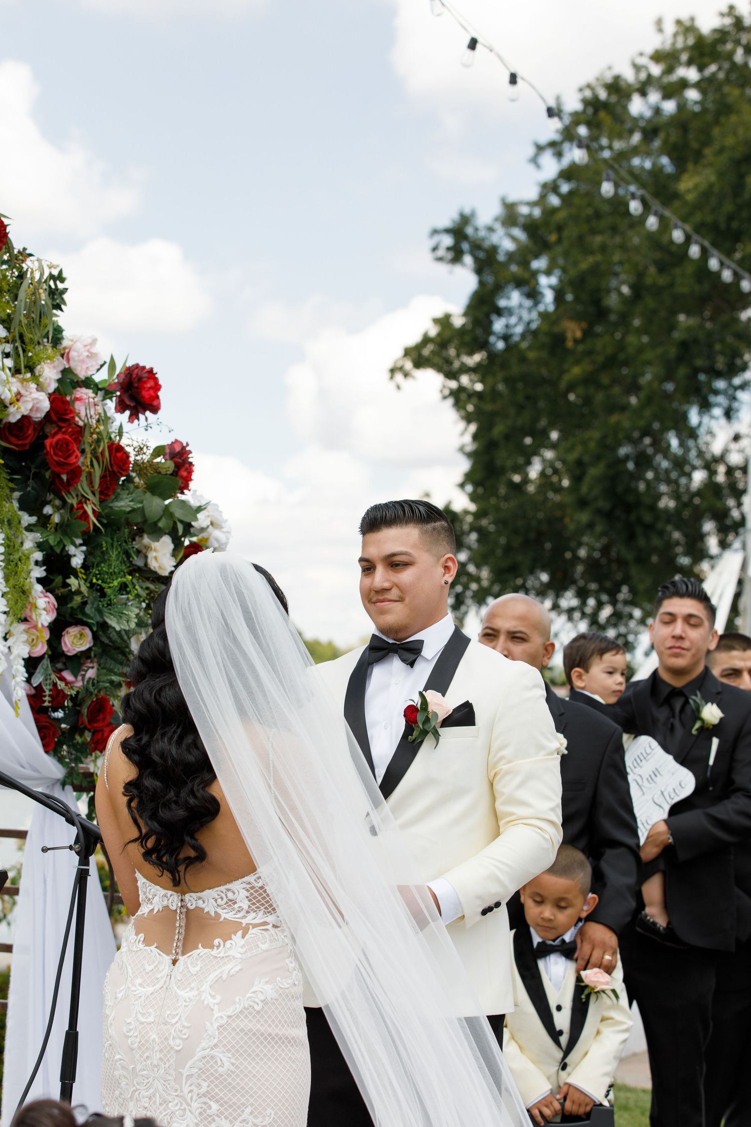 Wedding party celebrates outdoors with floral arrangements and formal attire on a bright sunny day.