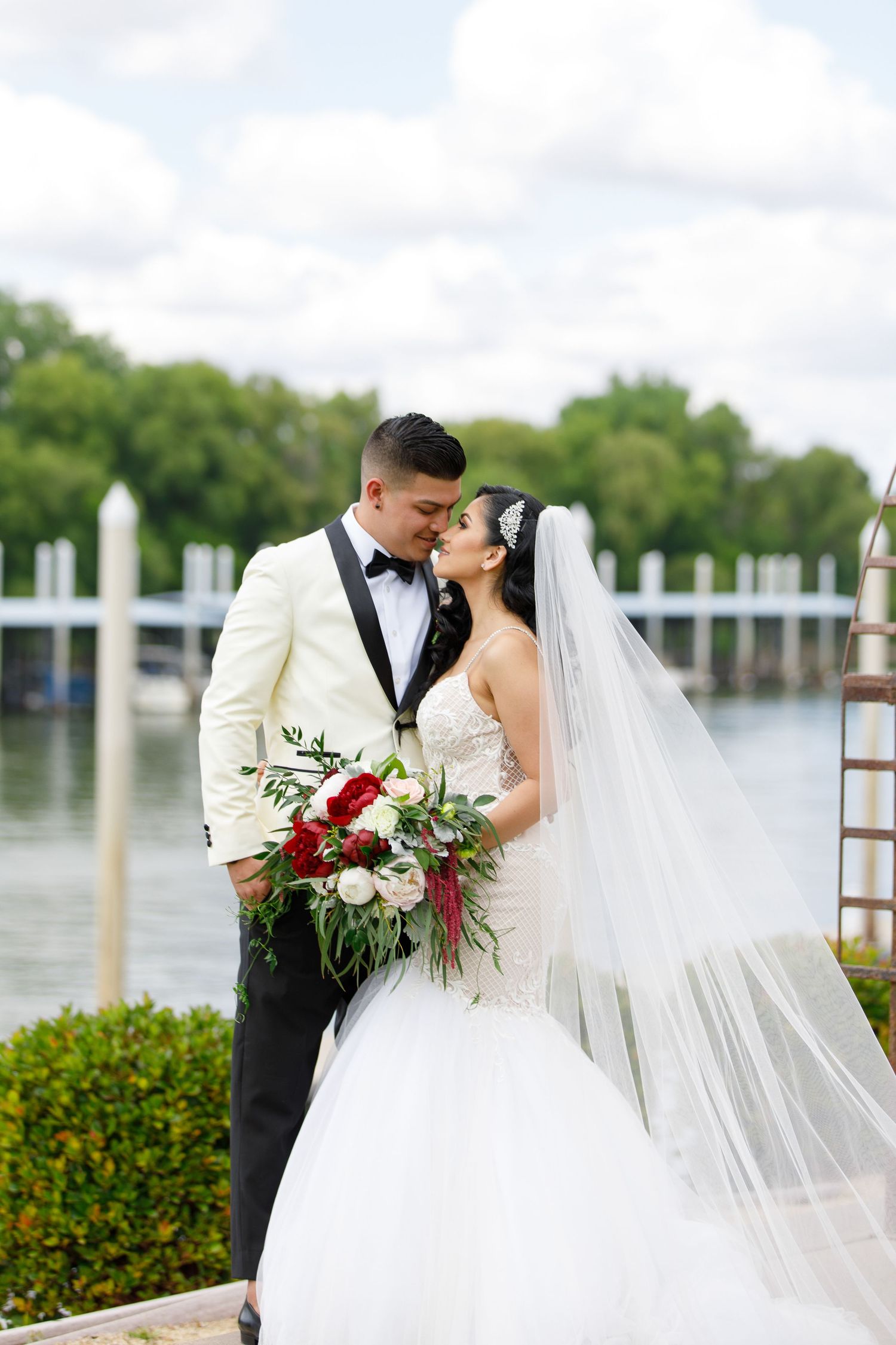 A romantic waterfront wedding scene with a couple sharing a kiss as the bride's veil flows in the breeze.