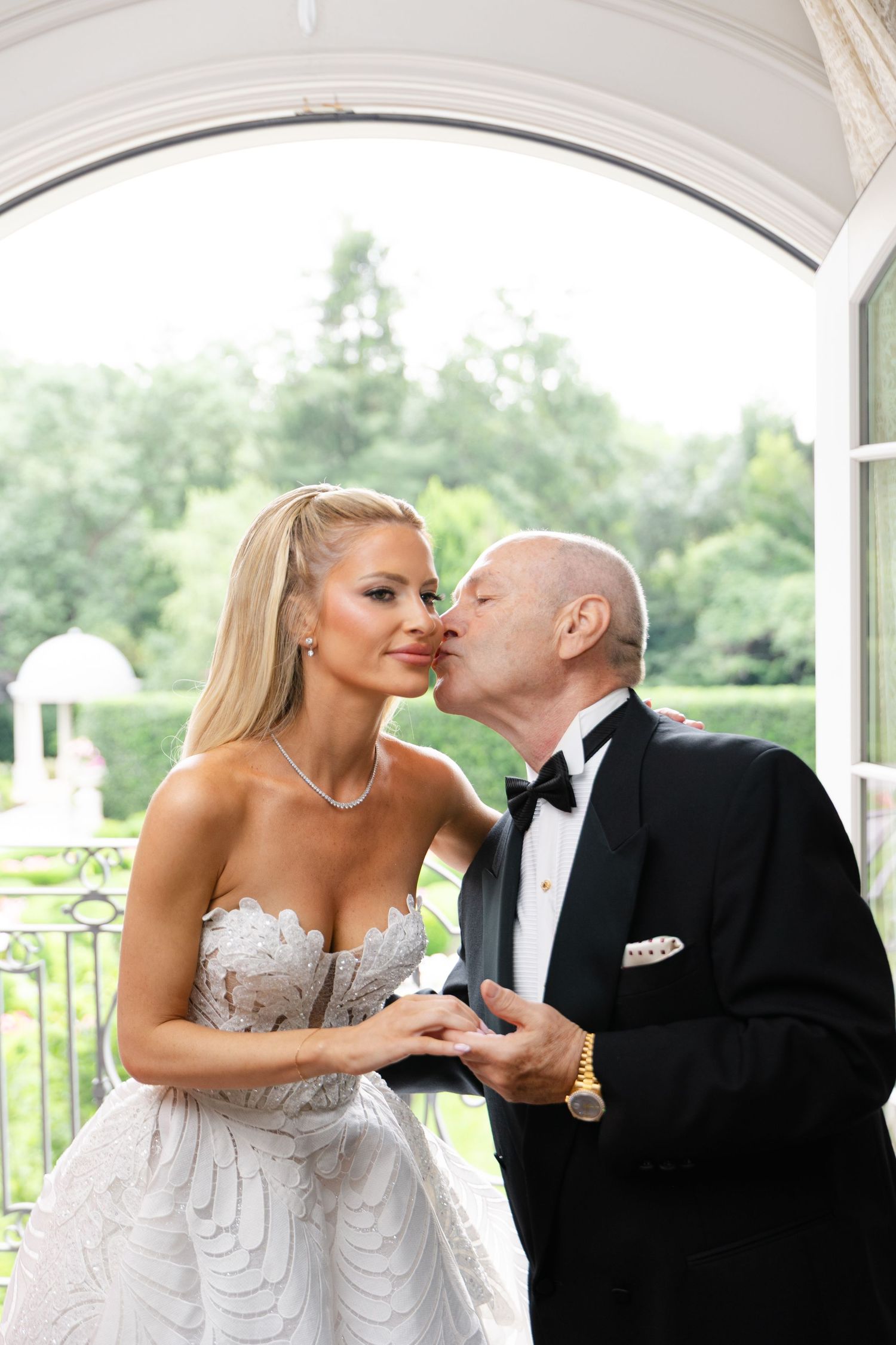 A tender moment shared between a bride in a strapless white gown and someone in a black tuxedo on their wedding day.