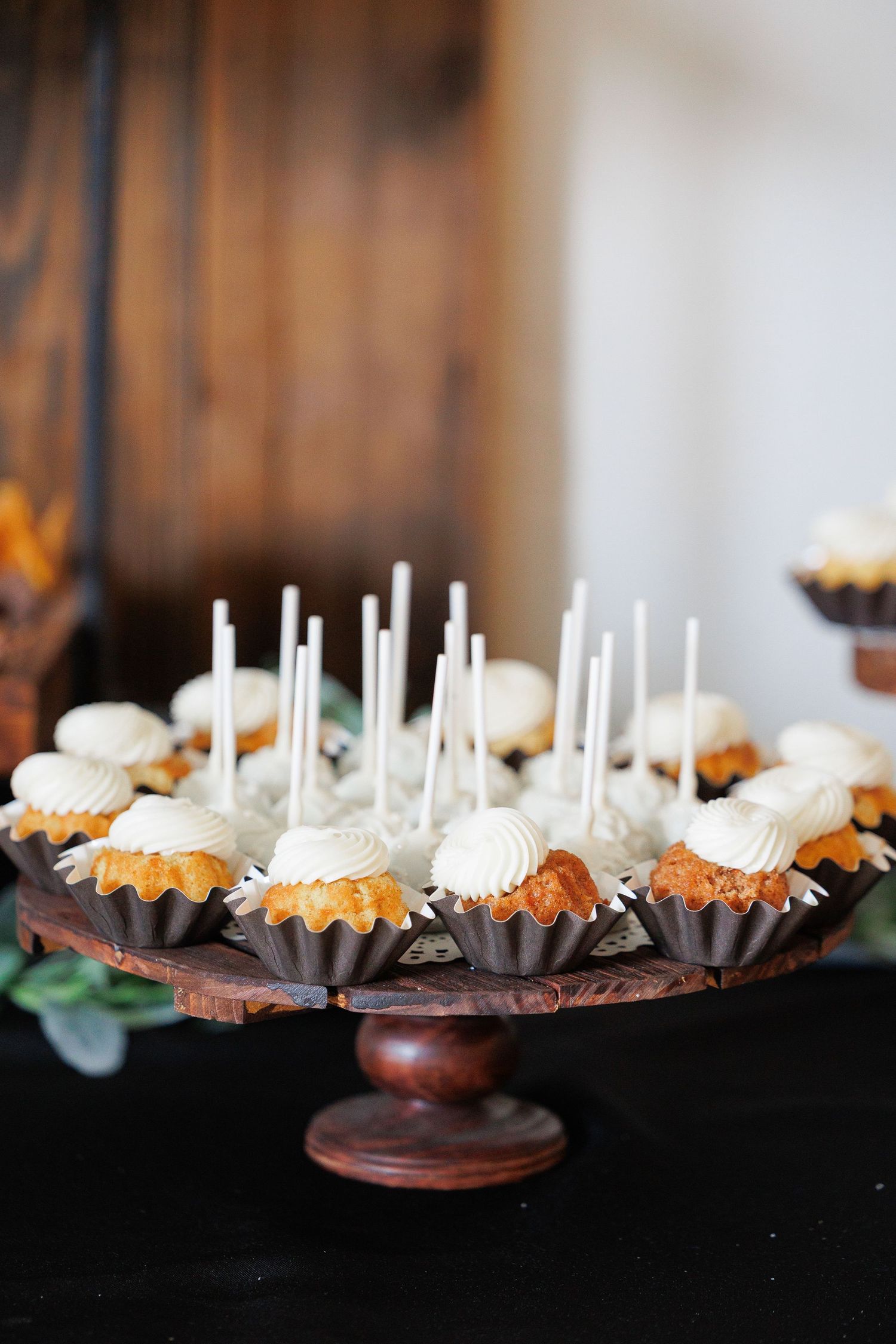 Elegant dessert platter featuring chocolate-dipped cake pops with white sticks arranged in rows on dark wooden stands.