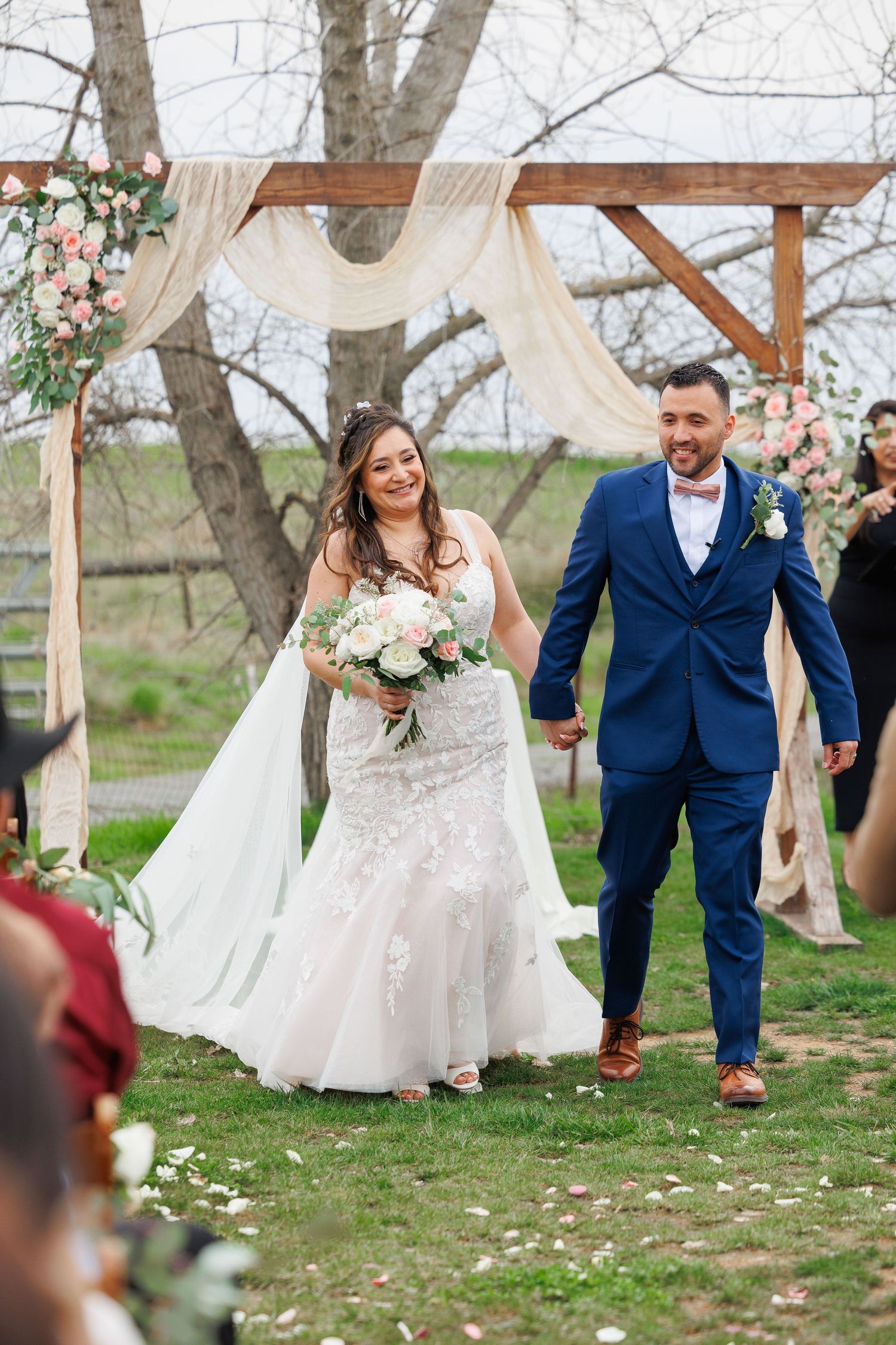 Couple celebrates joyfully during outdoor spring wedding ceremony under rustic wooden arch with floral decorations.