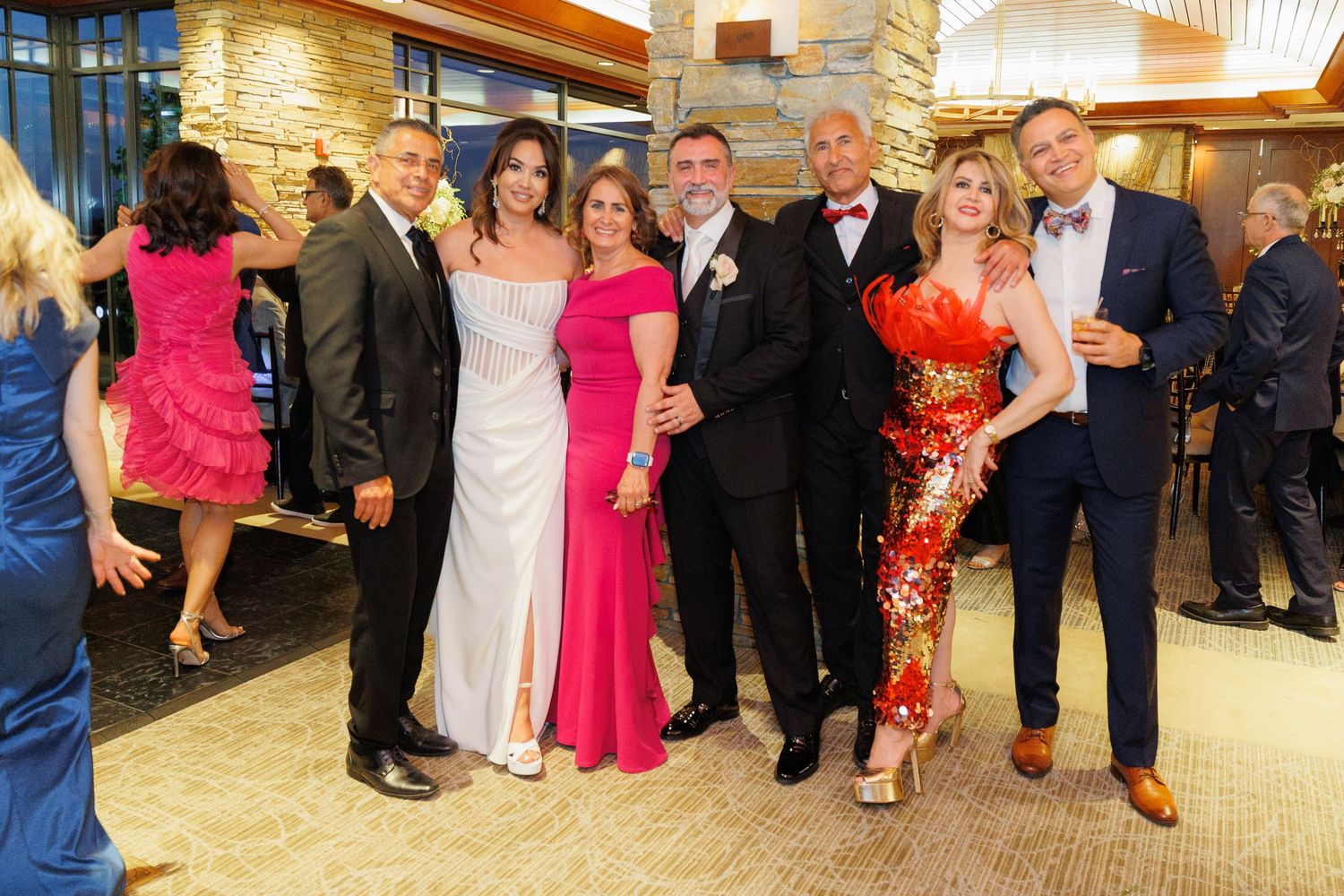 A group in formal attire poses together at an elegant event with stone walls and warm lighting in the background.