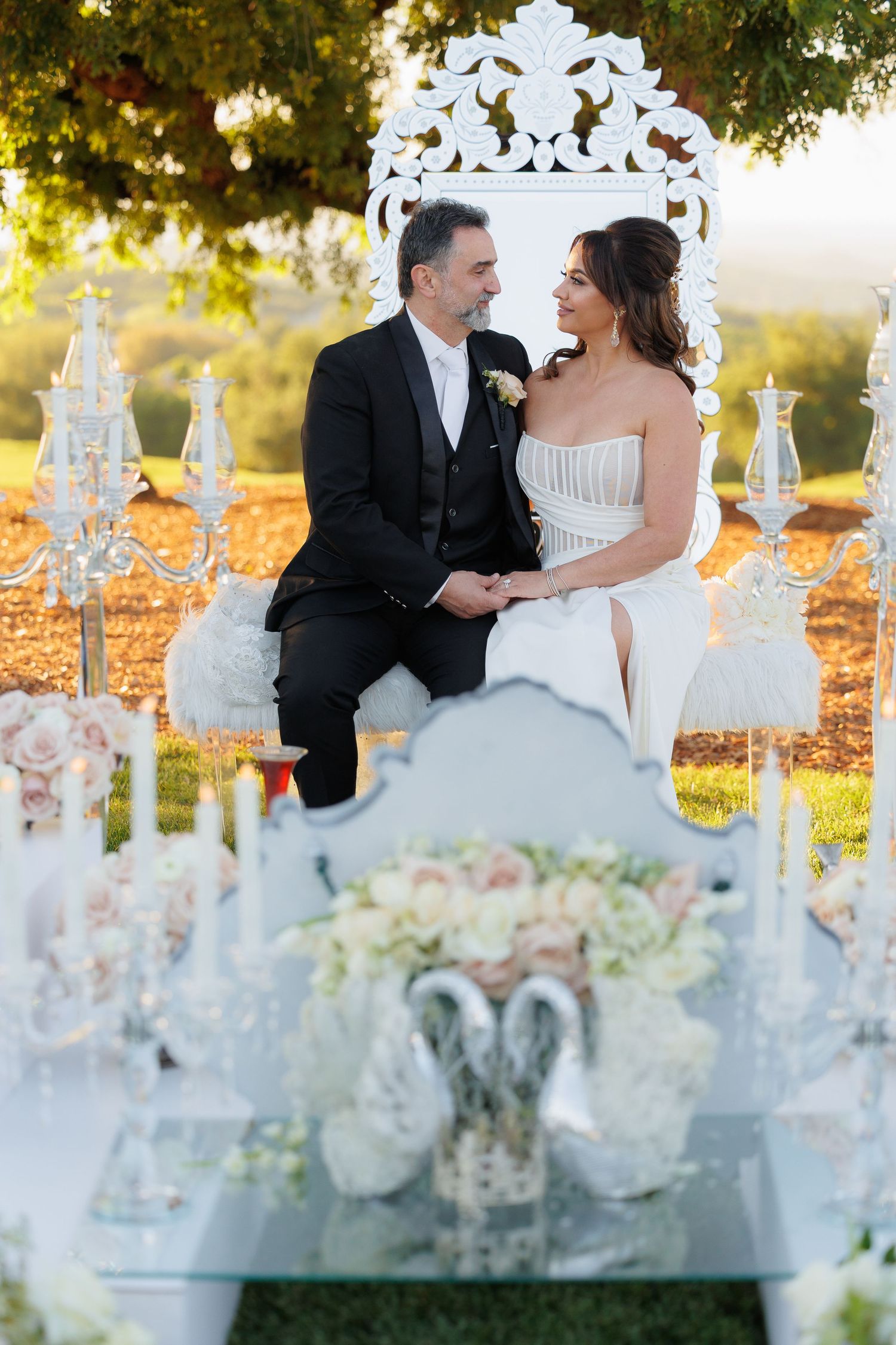 Elegant wedding reception table decorated with white floral arrangements and crystal candelabras in an outdoor garden setting.
