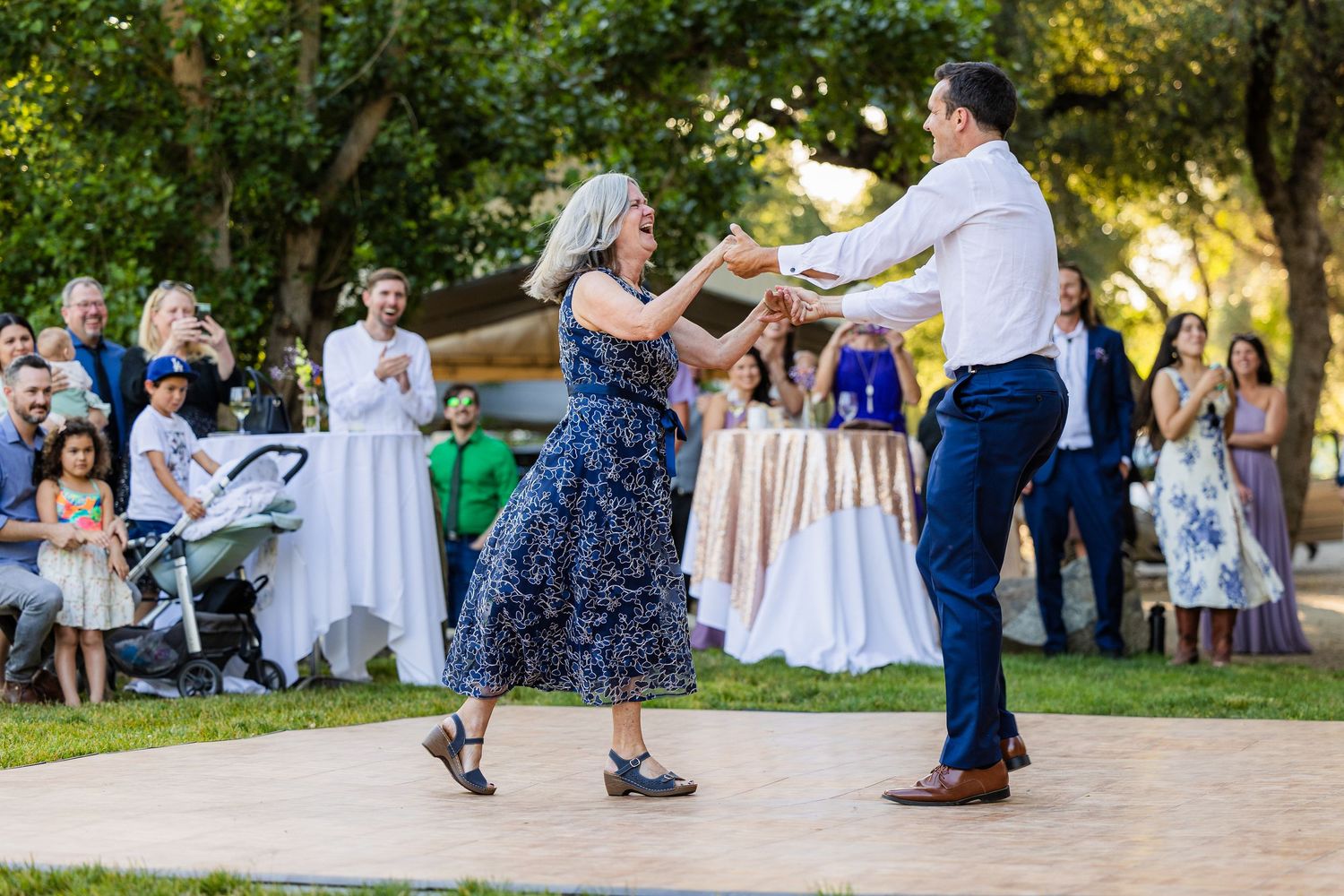 People dancing together at an outdoor wedding reception during golden hour.