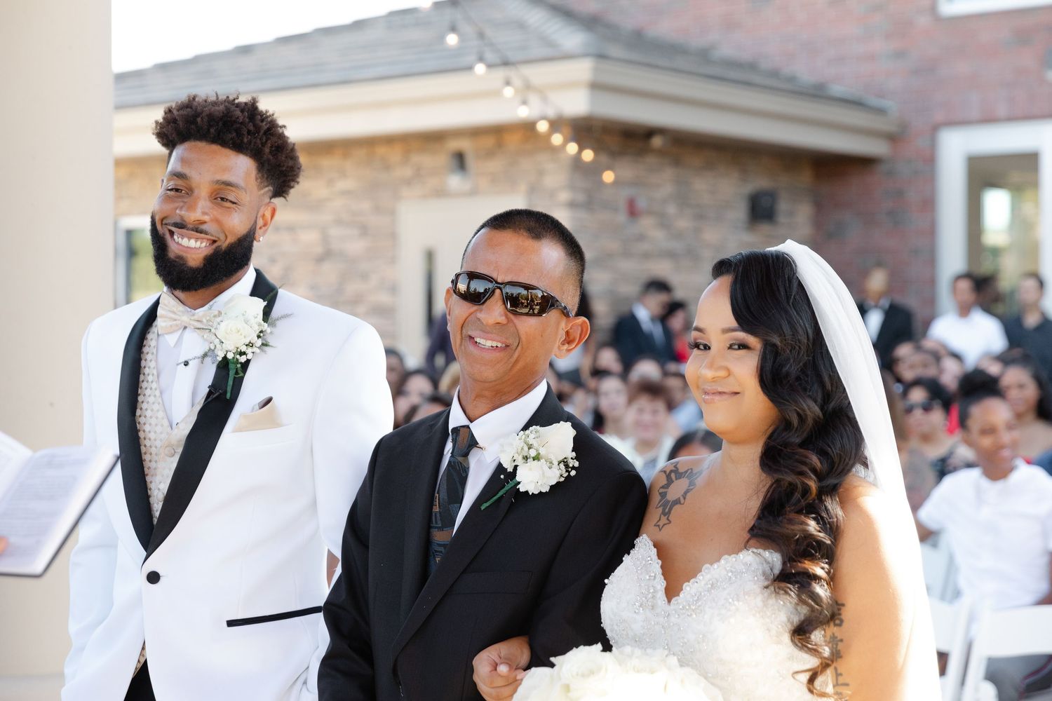 A wedding ceremony scene with guests seated outdoors and people in formal attire standing at the front.