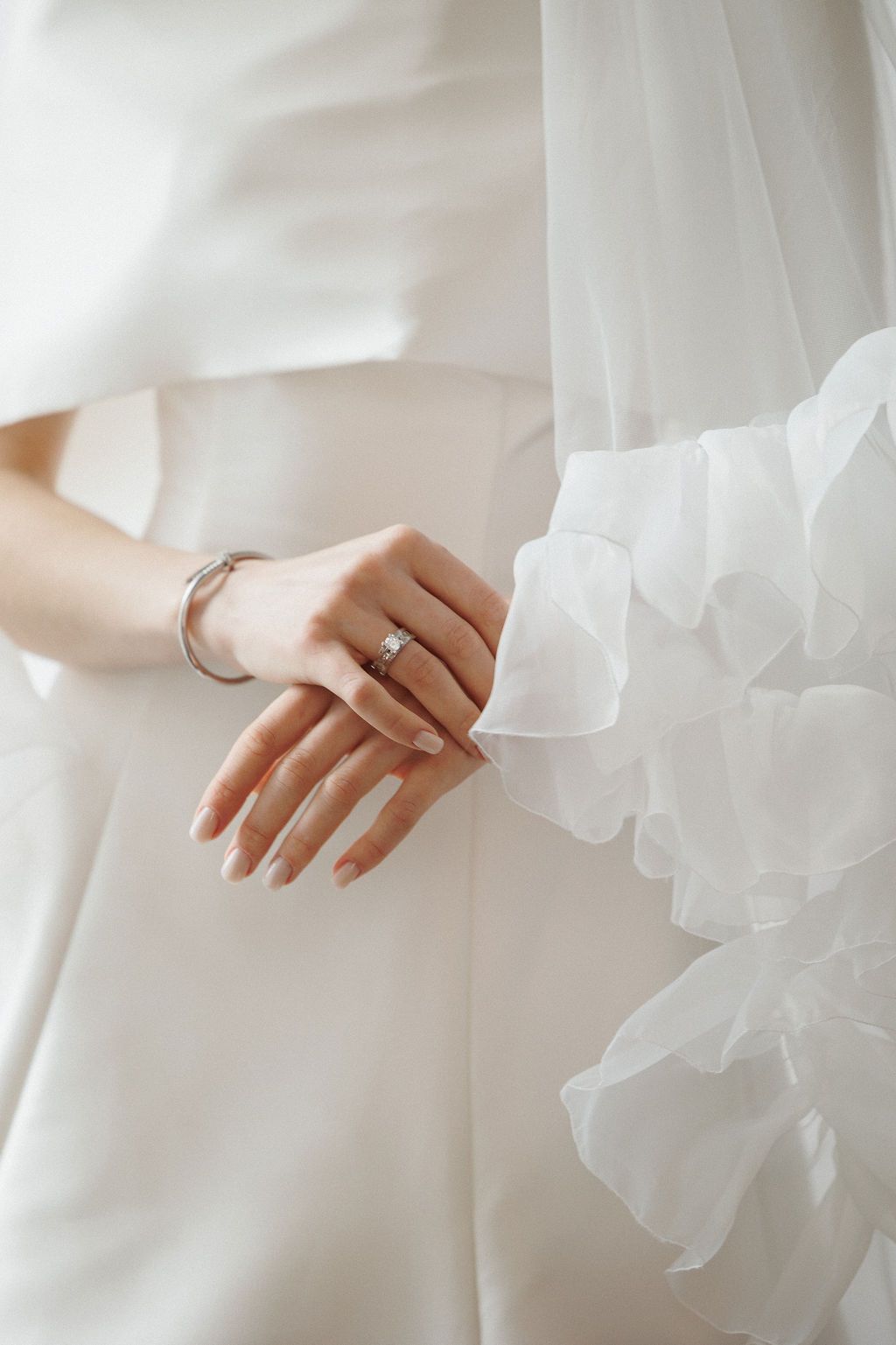 Close-up of a delicate hand wearing an engagement ring with flowing white fabric details.