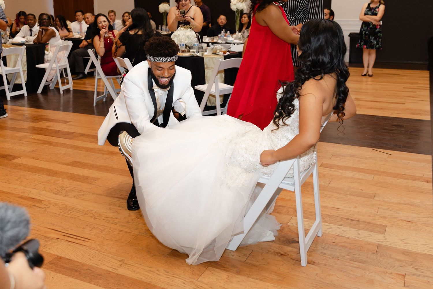 Guests enjoy a wedding reception in an elegant venue with hardwood floors and white chairs.