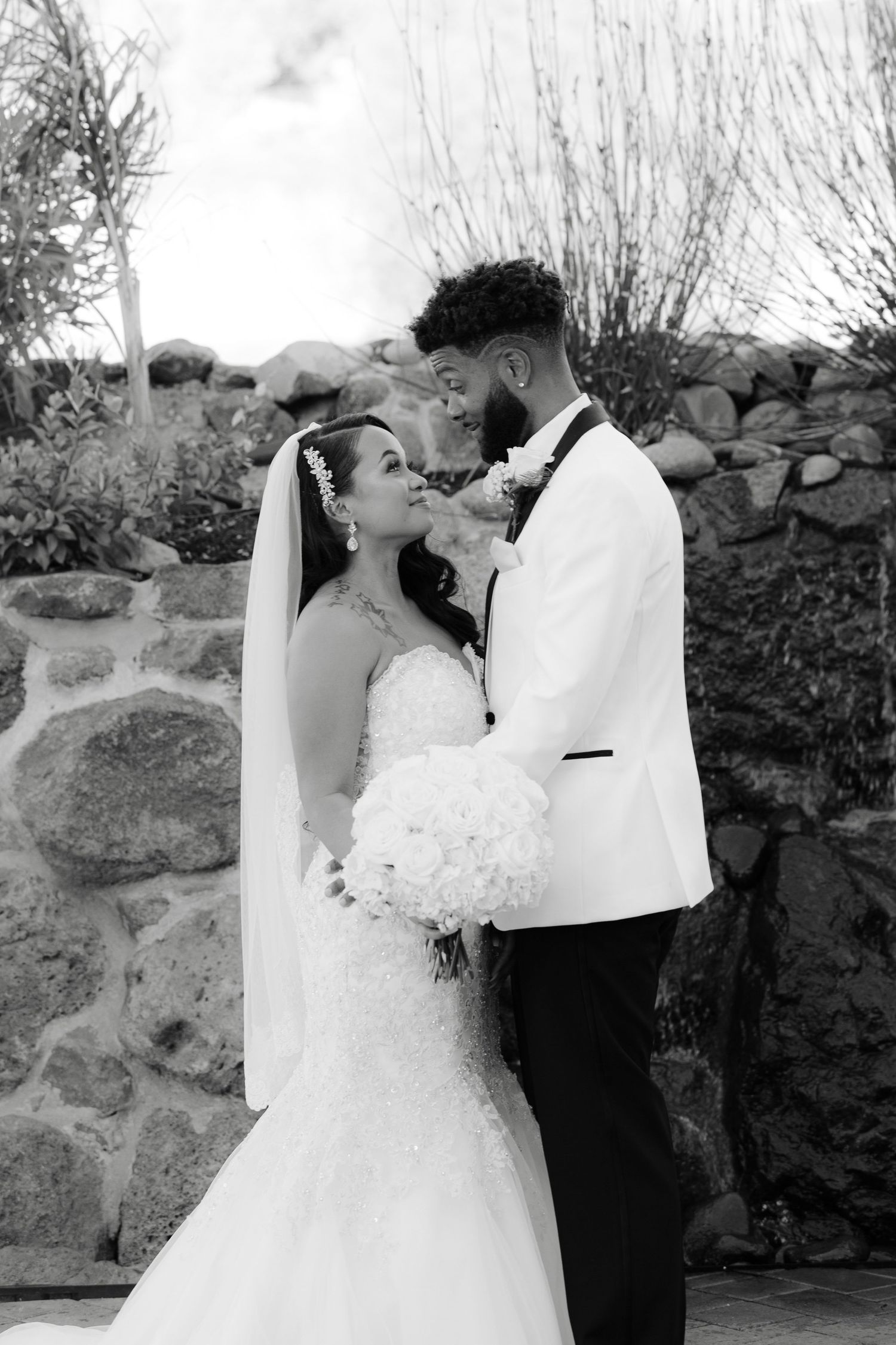 A romantic black and white wedding photo series showing a couple embracing against a stone wall backdrop.