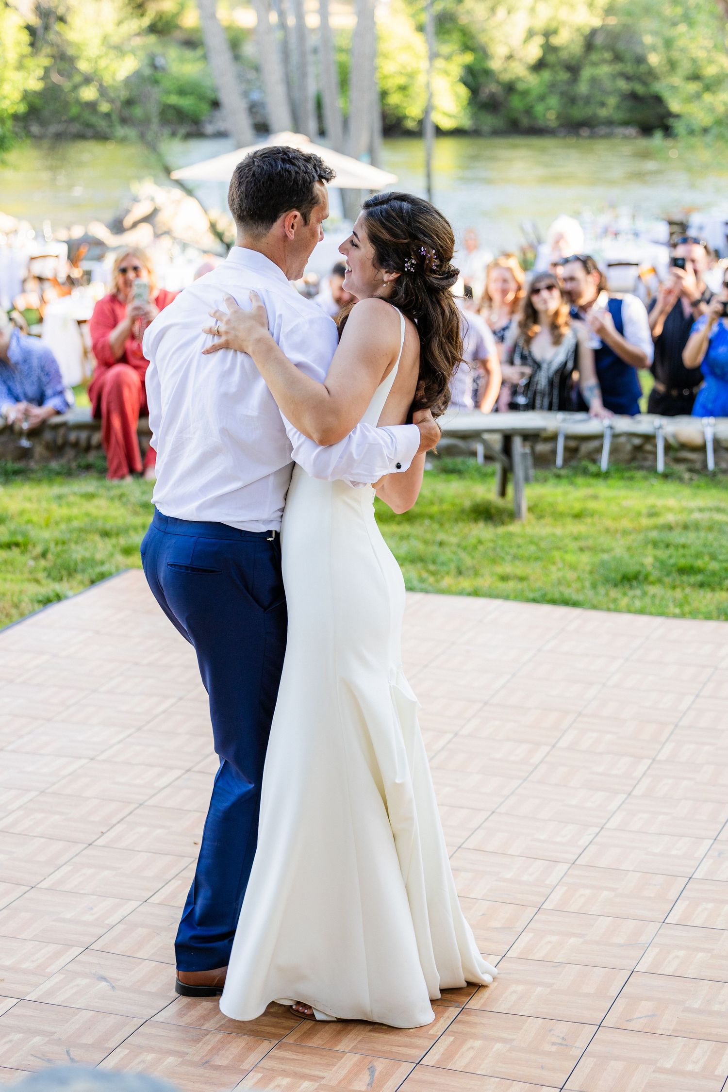 A couple in wedding attire dances together on an outdoor patio during their wedding reception celebration.