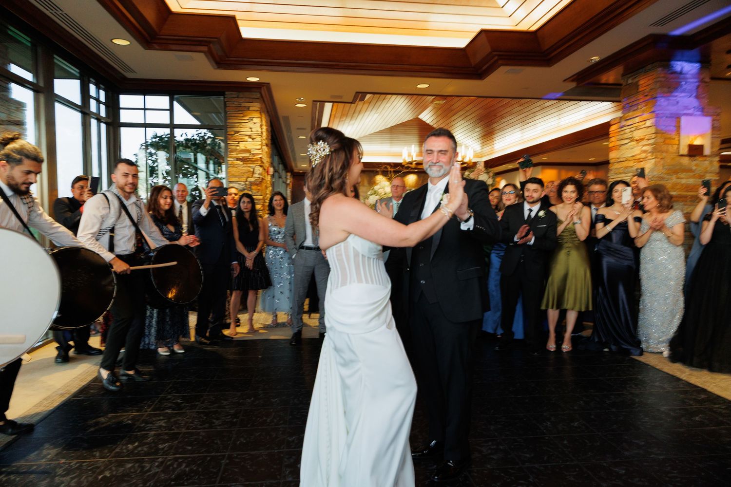 Wedding guests gather on a dance floor during a reception celebration at an elegant indoor venue.