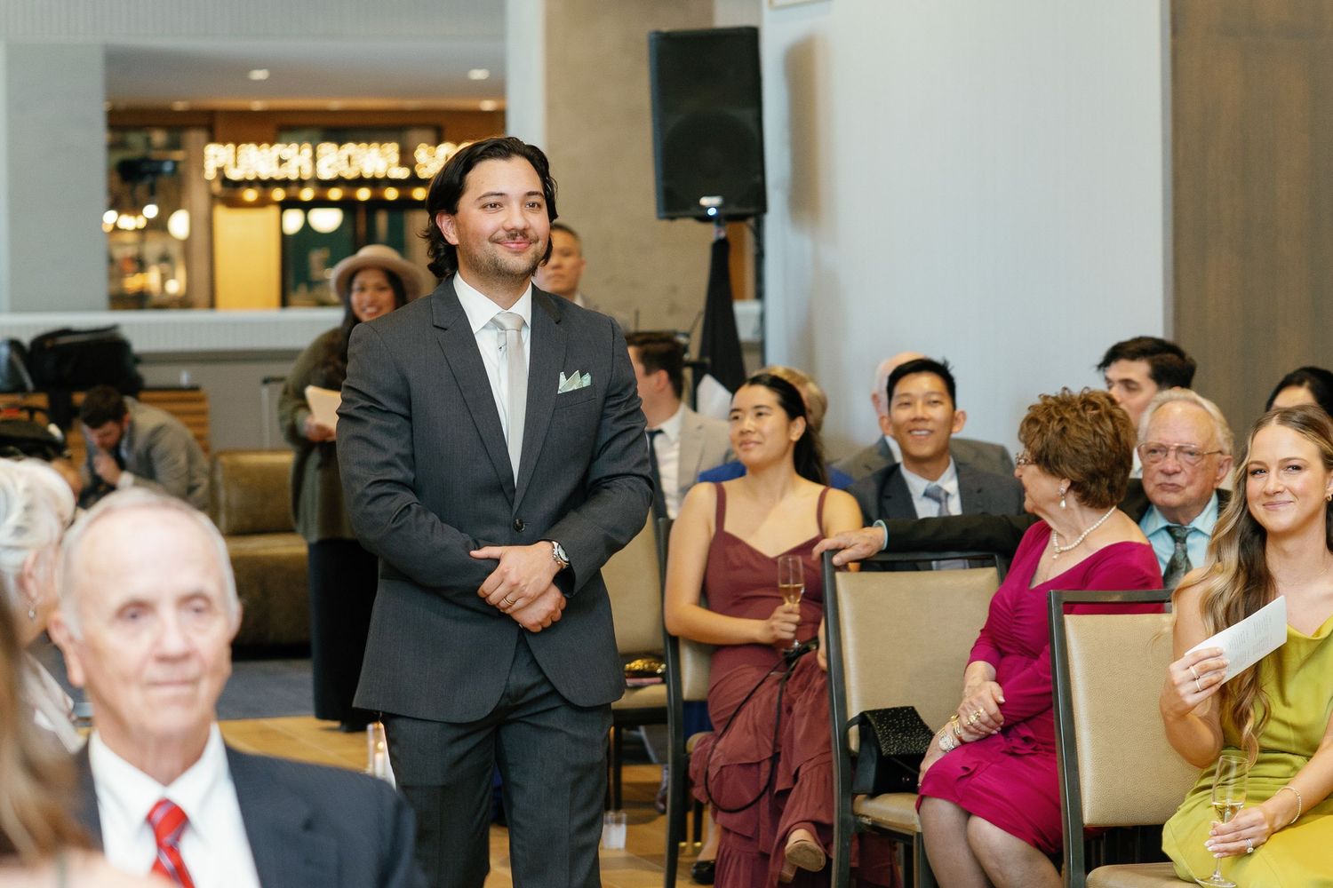 Wedding guests seated in rows watch attentively during an indoor ceremony at an elegant venue.