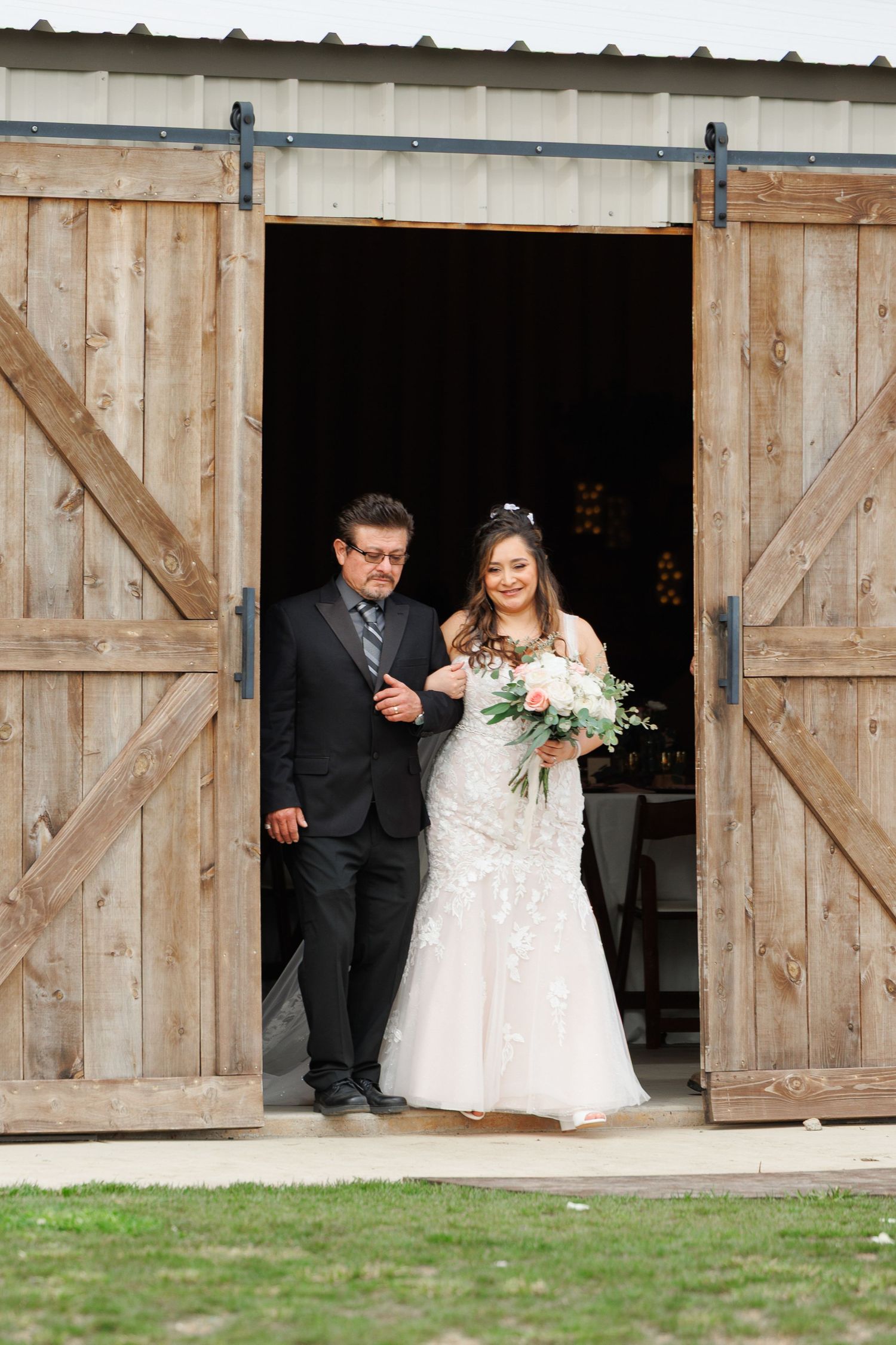 A couple stands in the doorway of a rustic wooden barn, with the bride holding a beautiful bouquet of flowers.