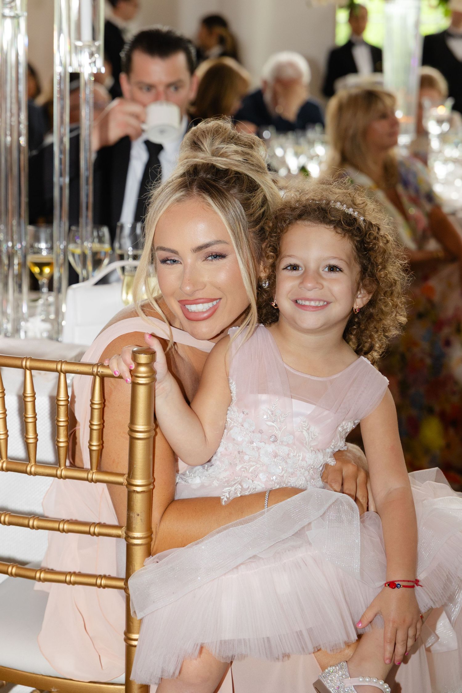 A woman and young girl in formal attire smile together at an elegant reception with gold chairs and table settings.