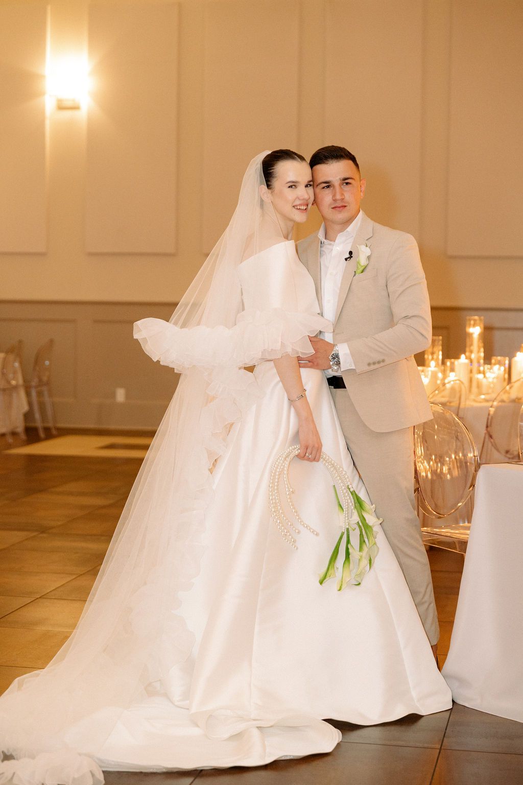 Elegant wedding photos featuring the couple in white and beige dancing in a warmly lit ballroom with candles.