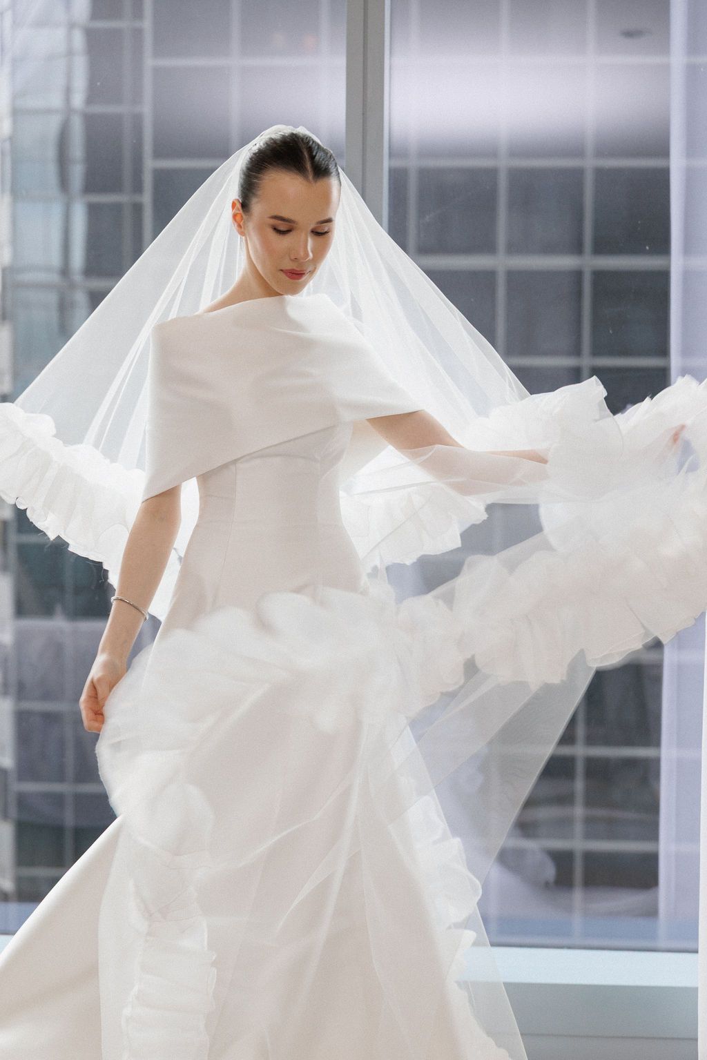 Ethereal bridal portraits showing flowing white veil and dress fabric in motion against modern windows.