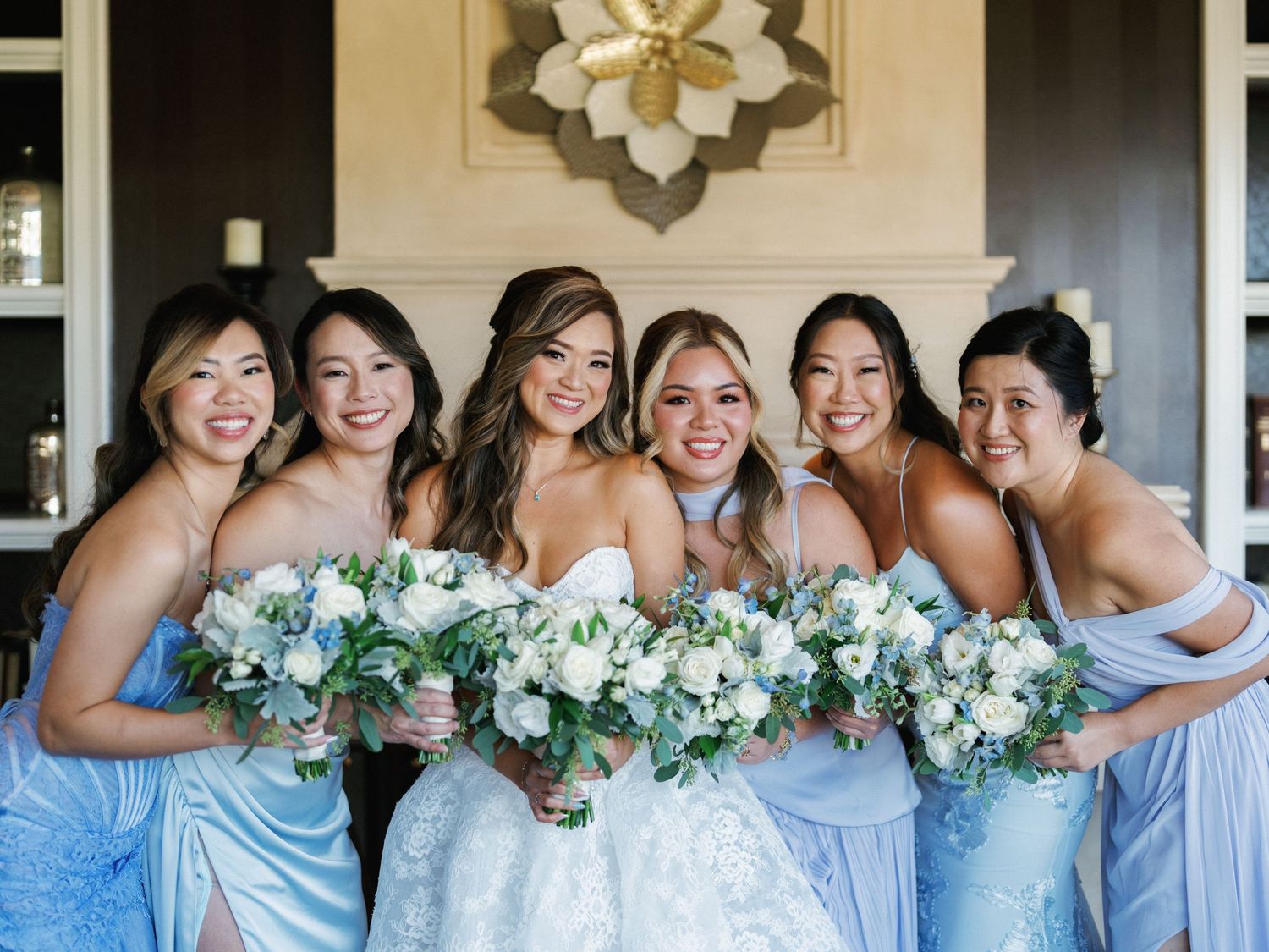 A row of bridesmaids in light blue dresses pose together while holding white and green floral bouquets.