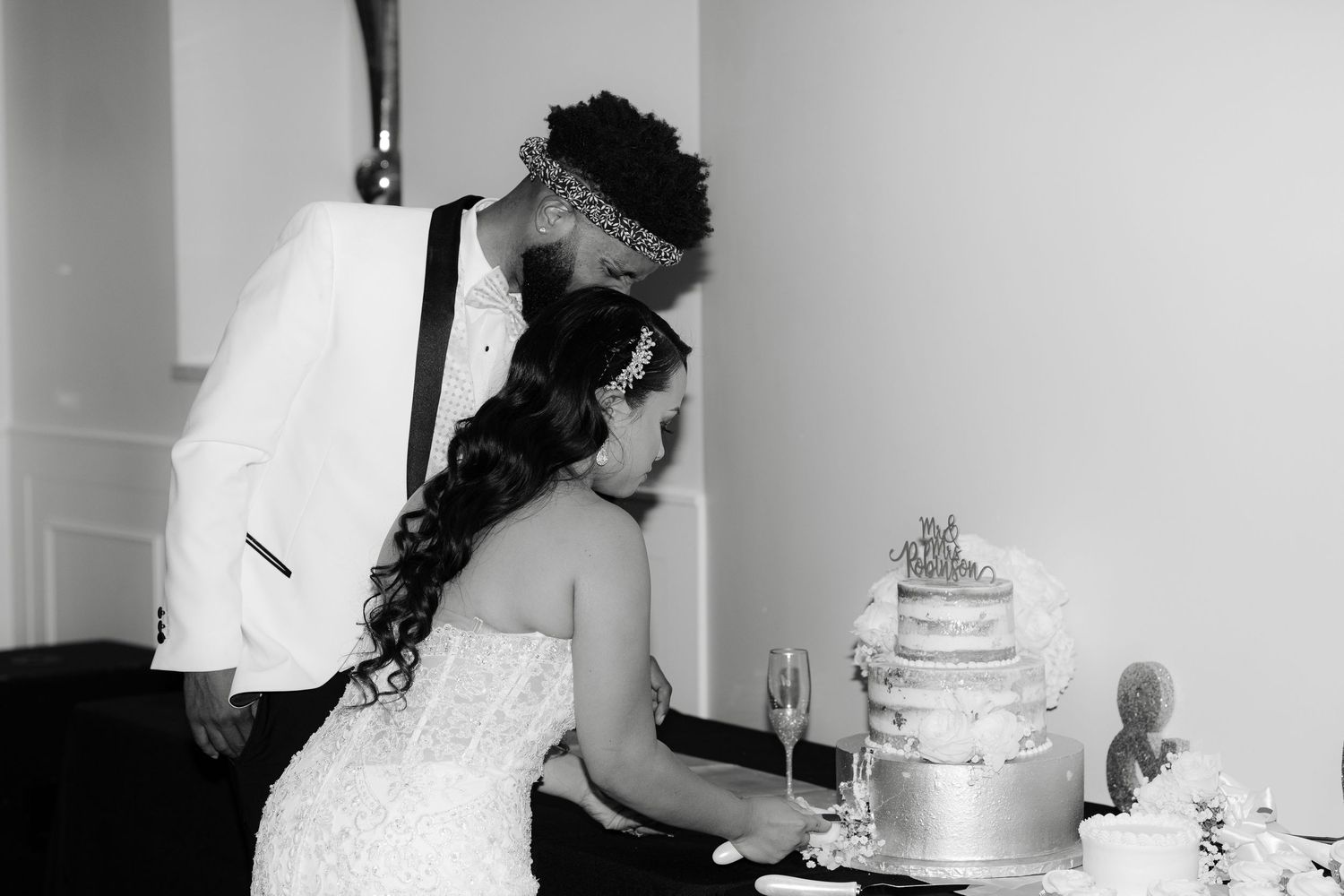 A black and white photo of a couple cutting their elegant tiered wedding cake together at their reception.
