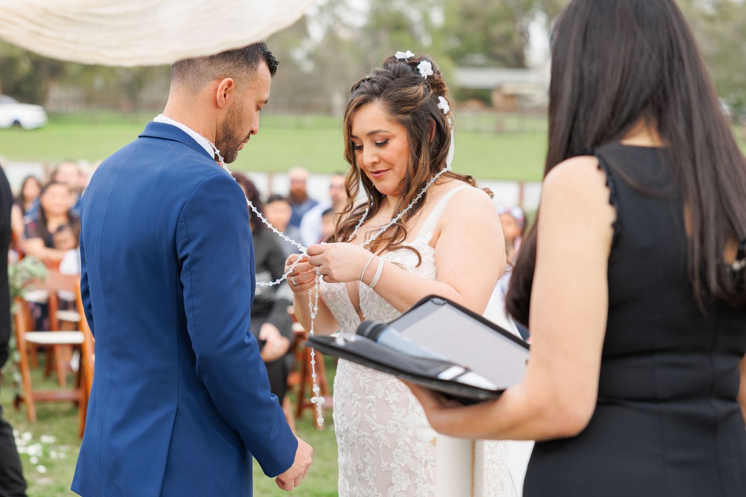 Guests sign a guestbook at an outdoor wedding ceremony while others wait in line.