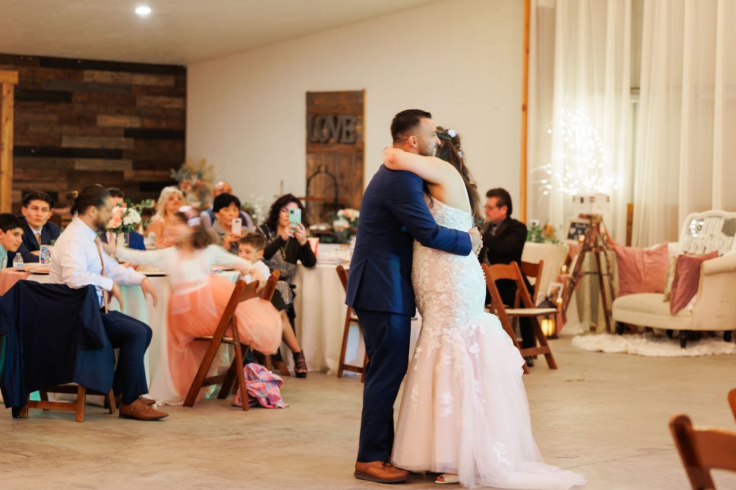 Wedding guests dance together in a reception hall with rustic wood accent walls and soft lighting.