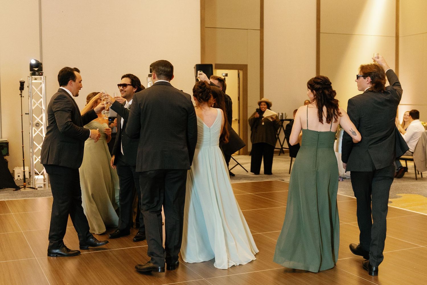 Wedding guests in formal attire dance and socialize on a wooden dance floor at an elegant reception venue.