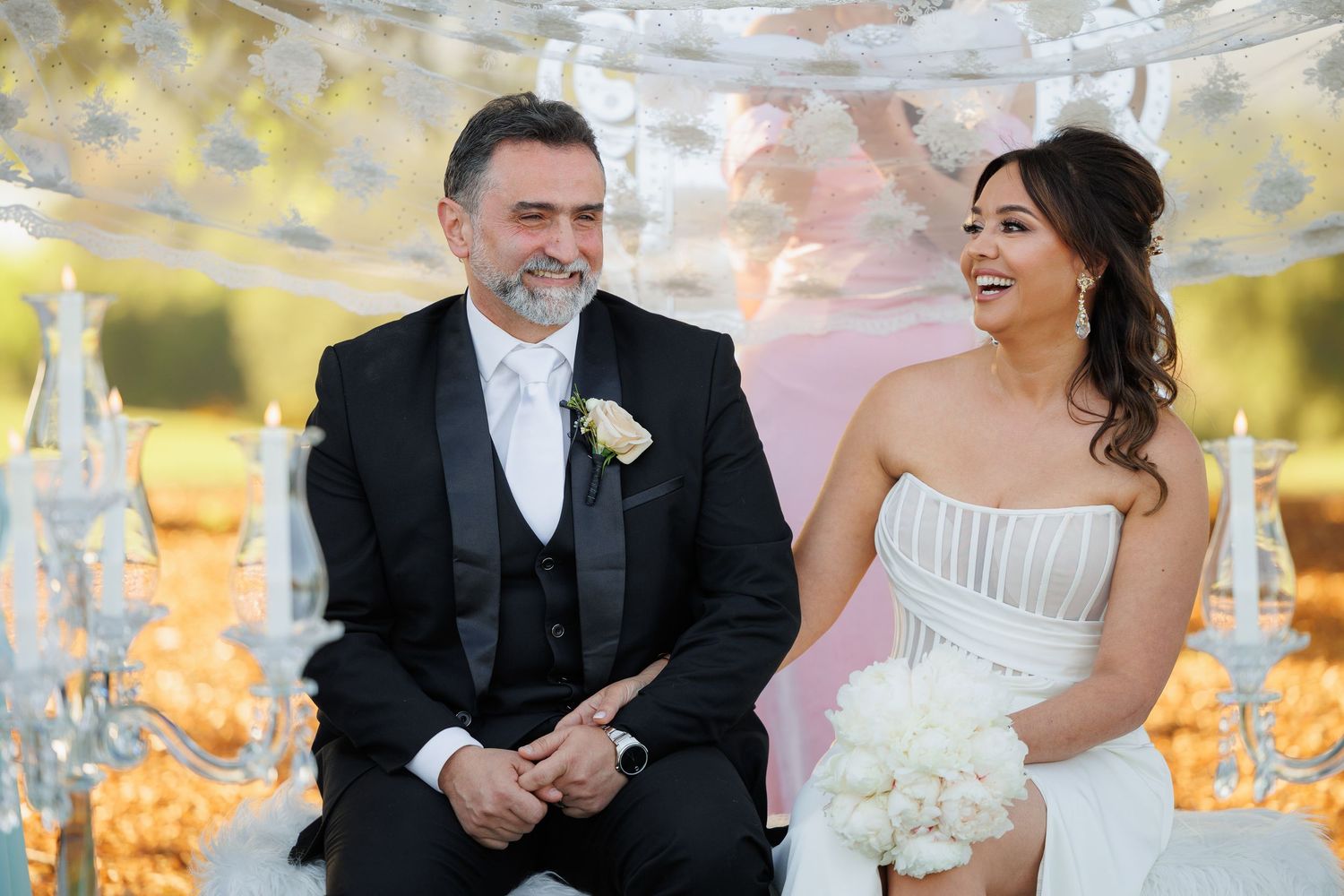 A joyful couple shares a candid moment of laughter during their outdoor wedding celebration.