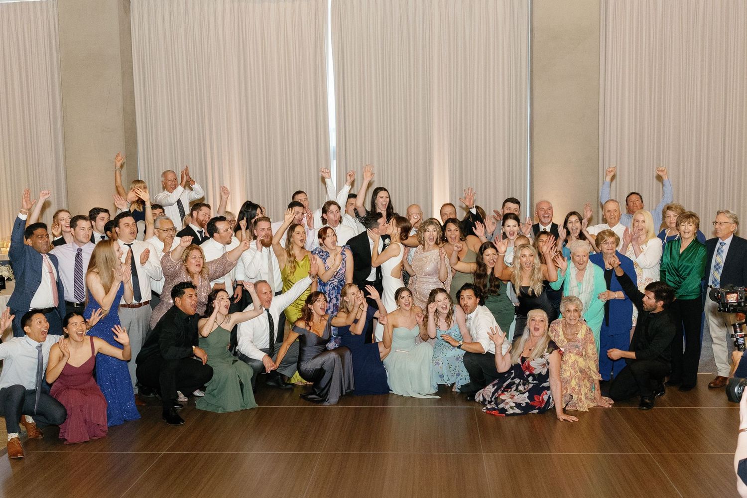 A panoramic view of wedding guests gathered in a large reception hall posing for a group photo.