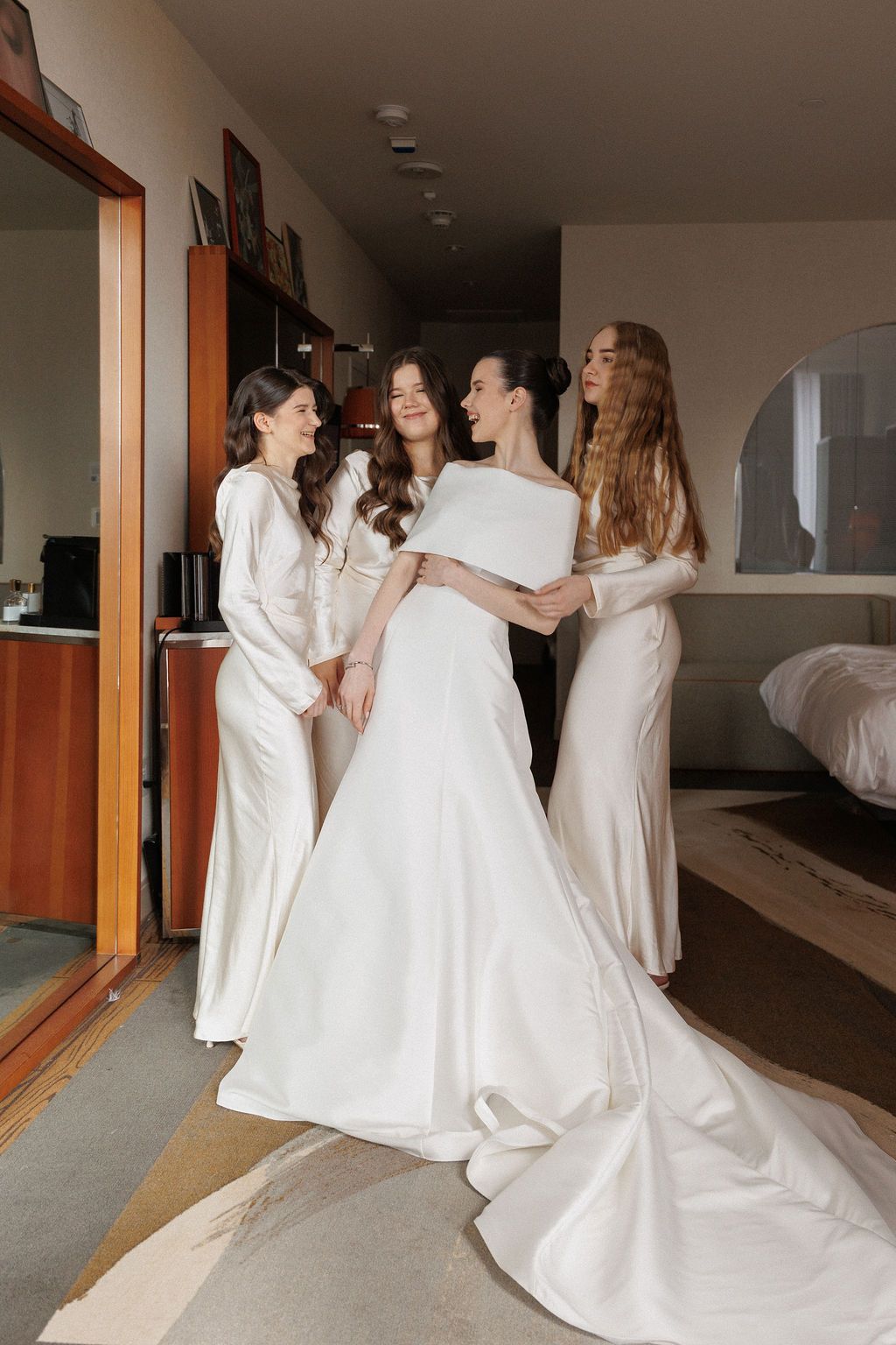 A group in elegant white dresses share a joyful moment together during wedding preparations.