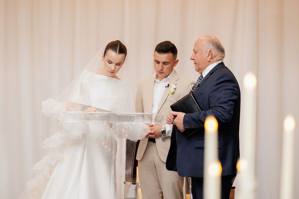 A romantic wedding ceremony moment with candlelight and white decor in an elegant ballroom setting.