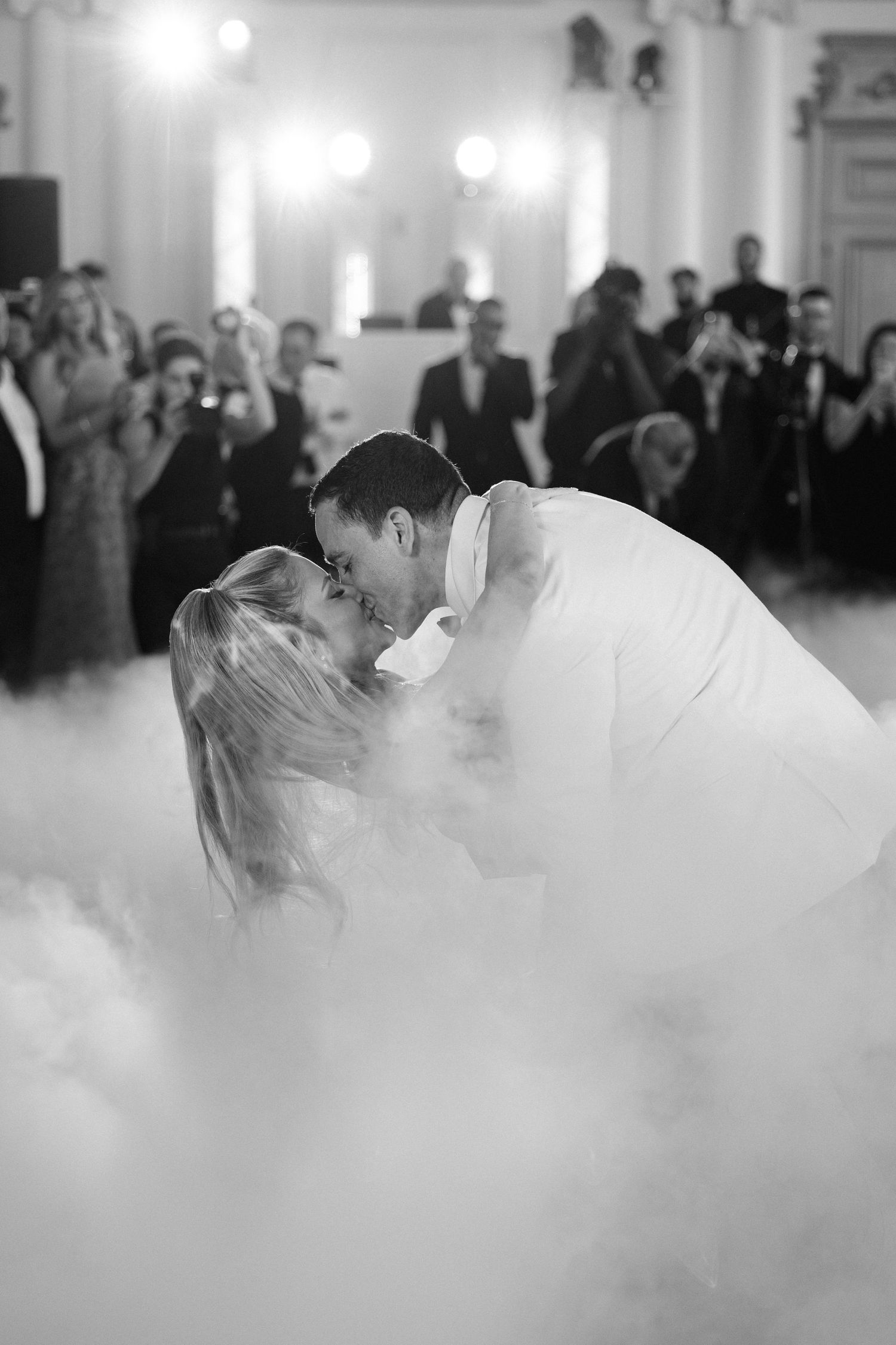 A couple shares their first dance as newlyweds surrounded by fog effects on a dance floor at their wedding reception.