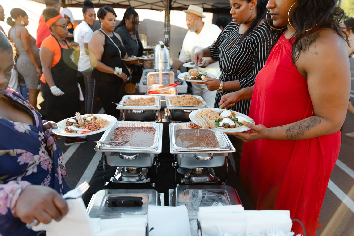 People enjoying food and drinks at an outdoor social gathering with tables set up for dining and refreshments.