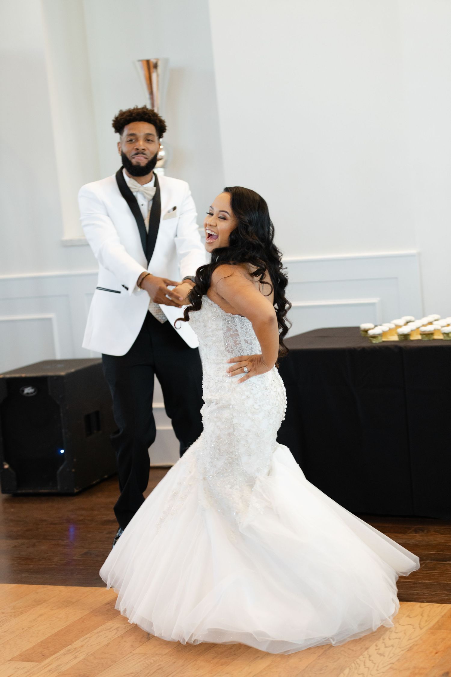 A couple in formal wedding attire dances together on a wooden floor during their reception celebration.