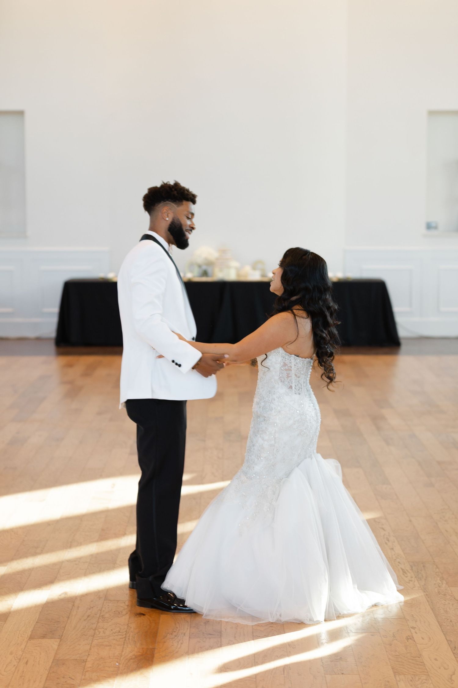 A couple shares their first dance at their wedding reception on a sunlit wooden dance floor.