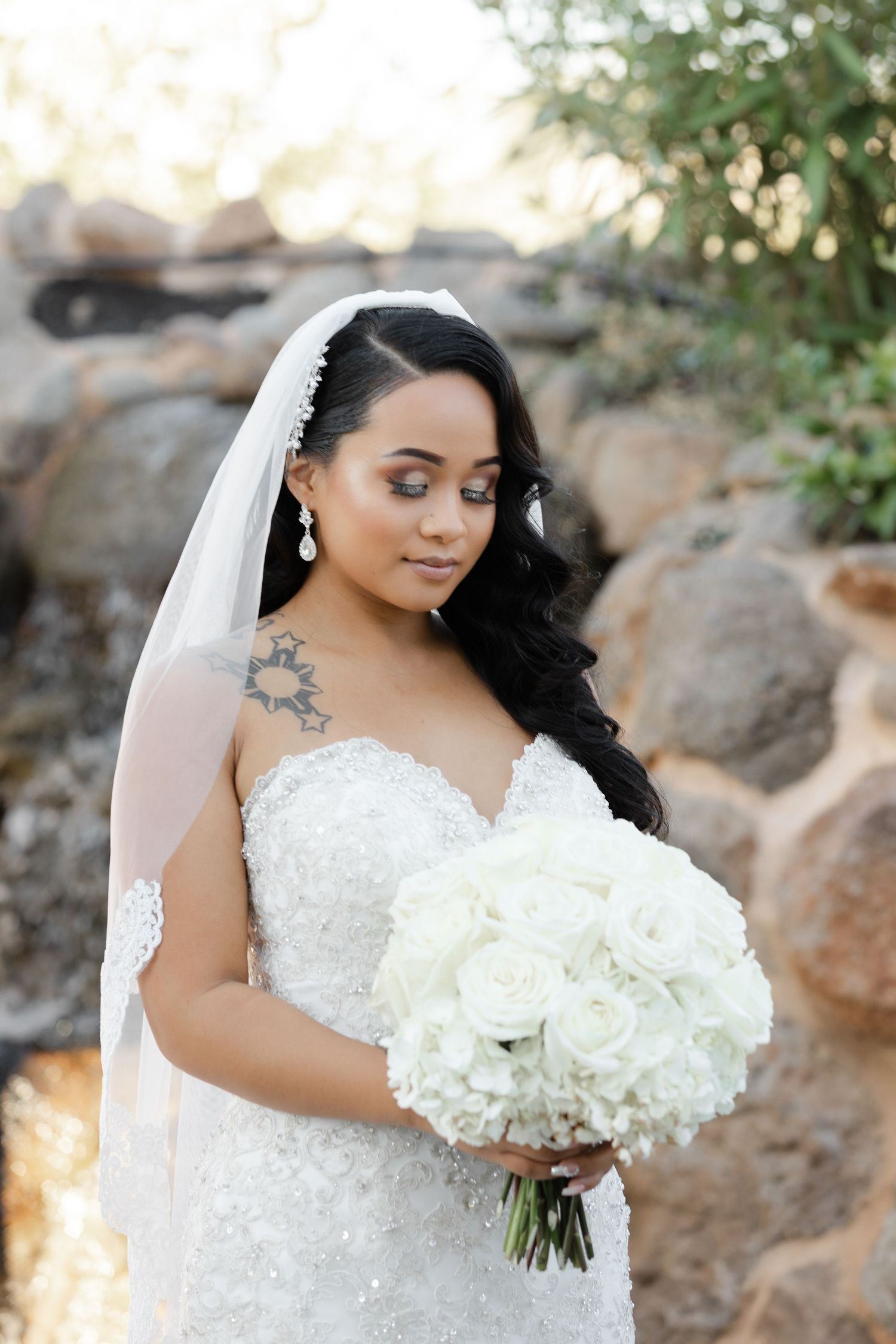 A bride in a white lace wedding dress holds a stunning bouquet of white hydrangeas against a natural outdoor backdrop.