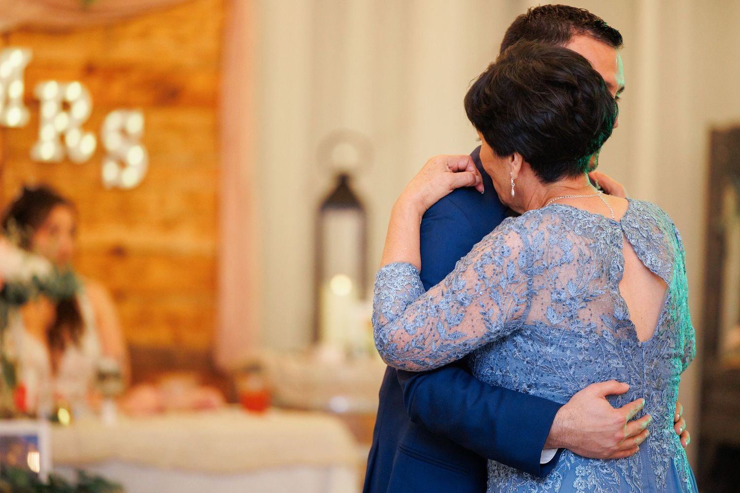 A couple shares an intimate embrace on their wedding day in a rustic wooden venue with warm lighting.