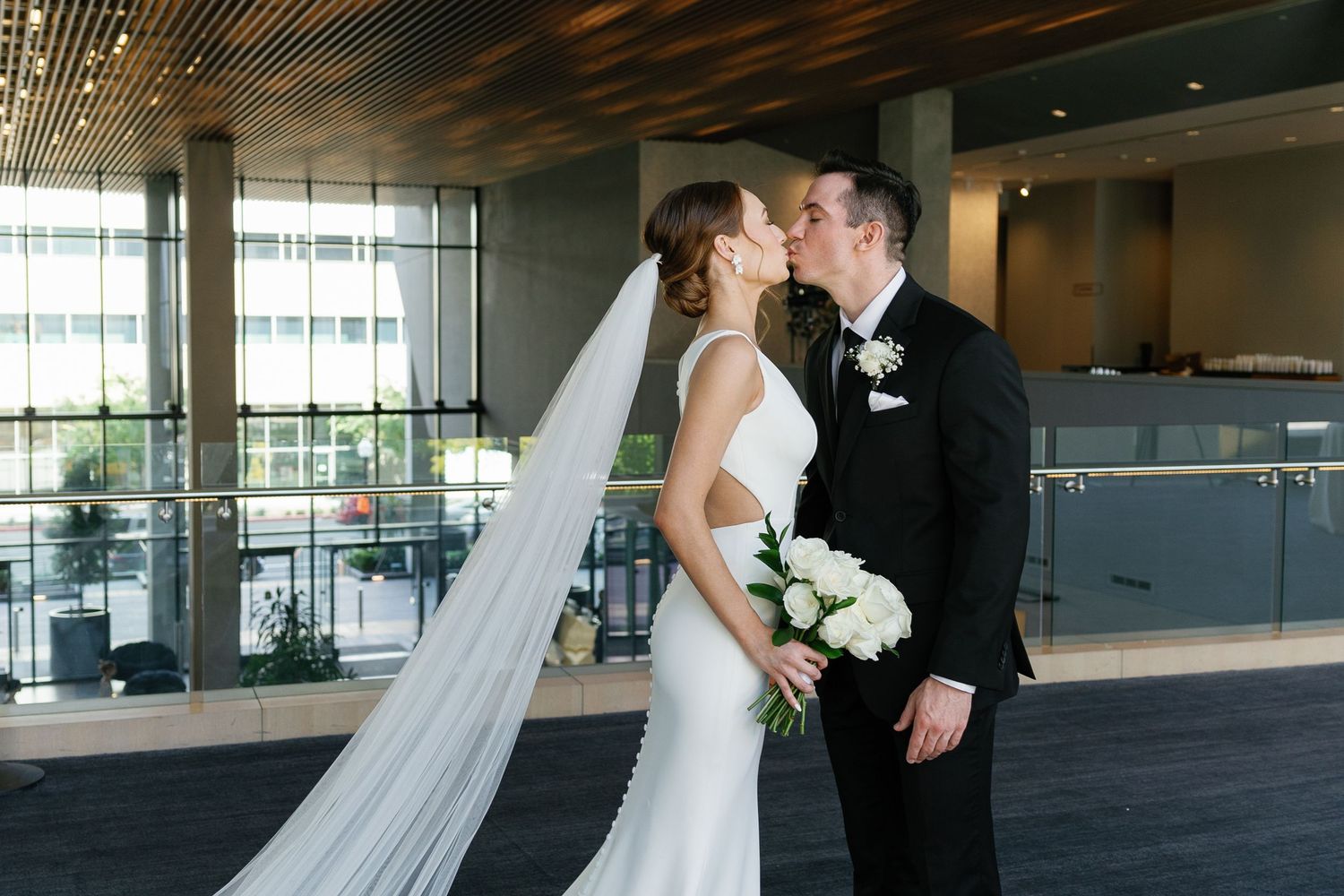 A couple shares a romantic moment in an elegant indoor venue with floor-to-ceiling windows.