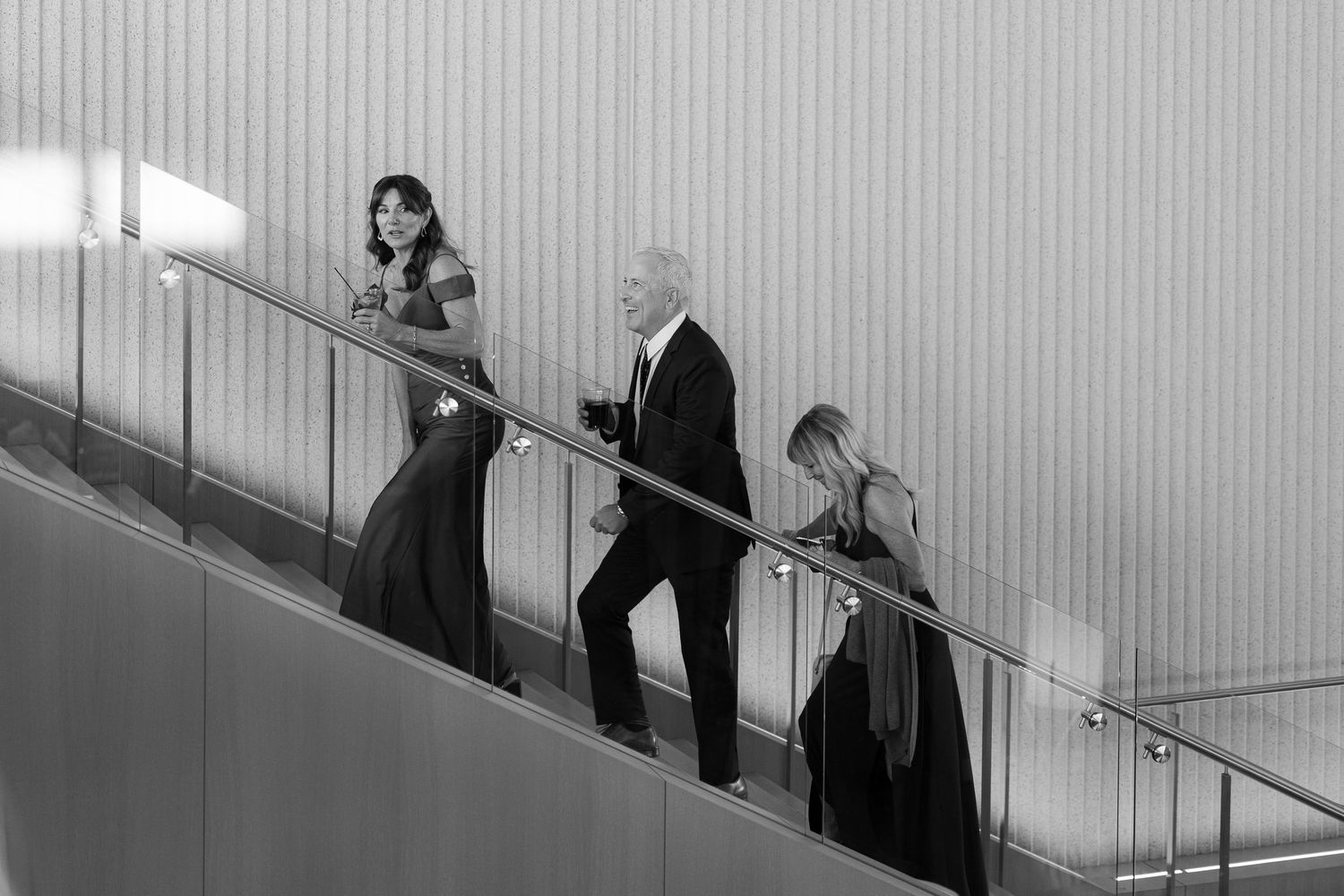 People descend a modern staircase in formal attire during what appears to be an event or gathering.