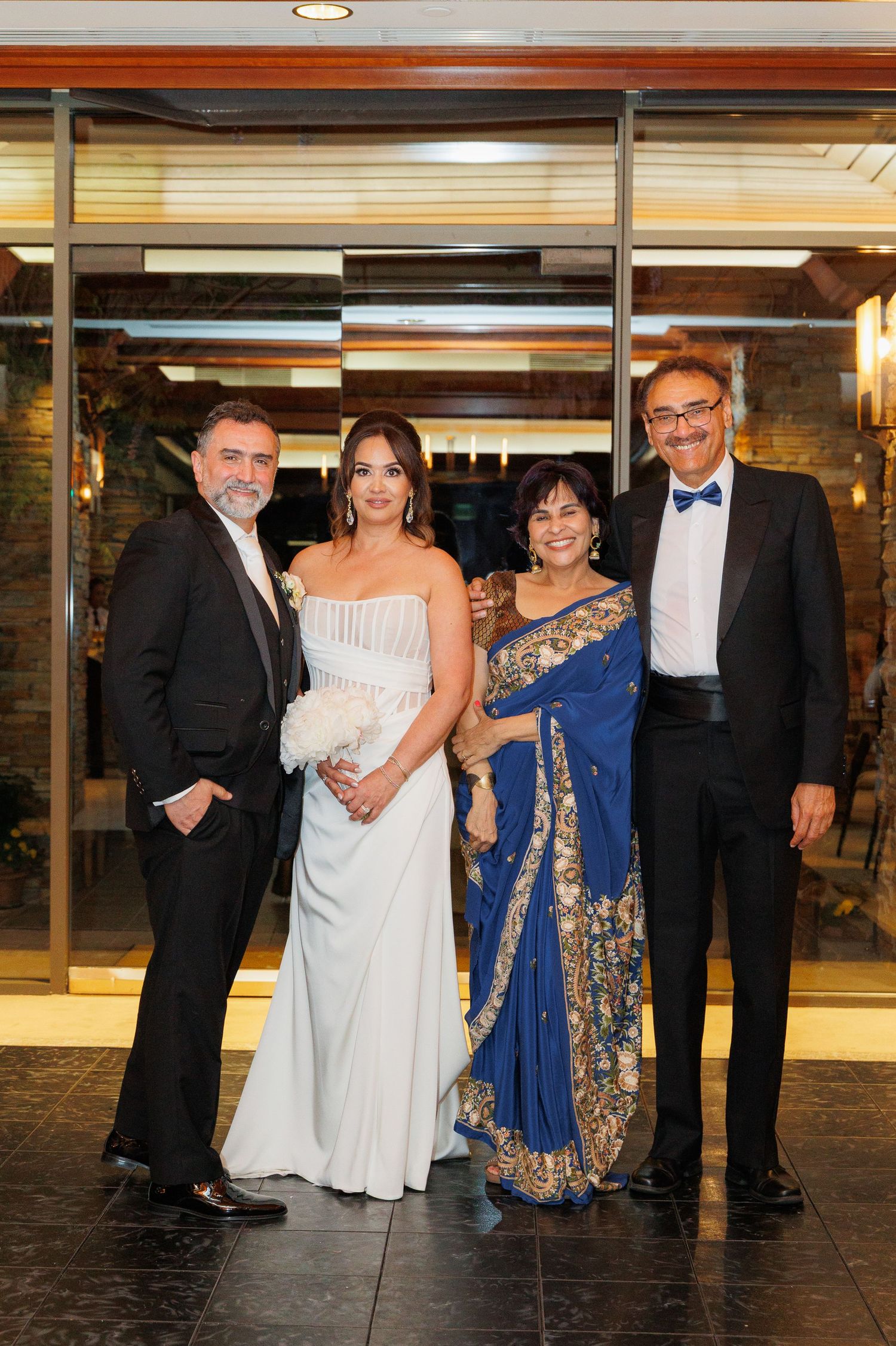 Group of formally dressed guests at an elegant event wearing evening attire and traditional Indian sari.
