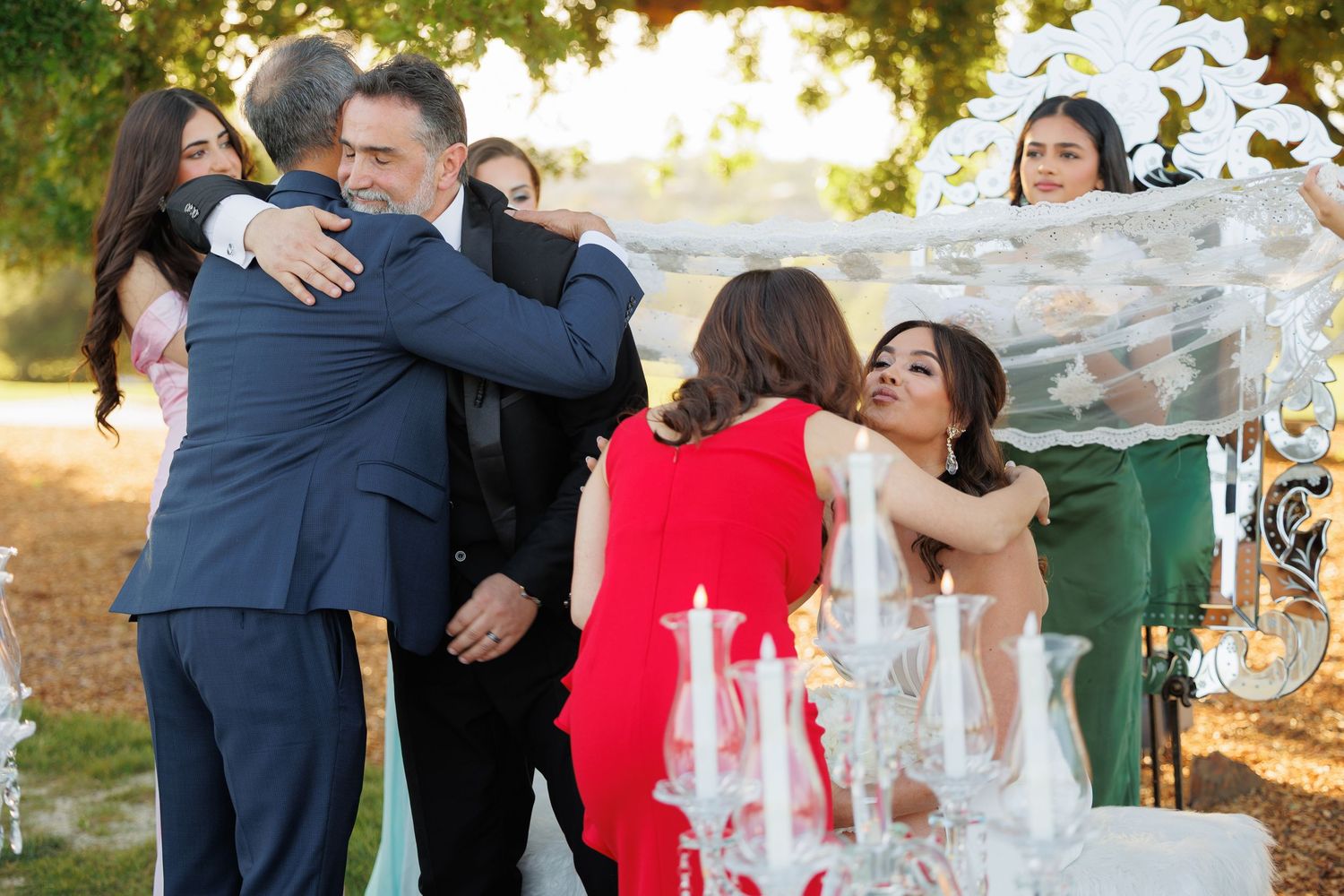 A group of people share joyful hugs and embraces during an outdoor celebration at sunset.
