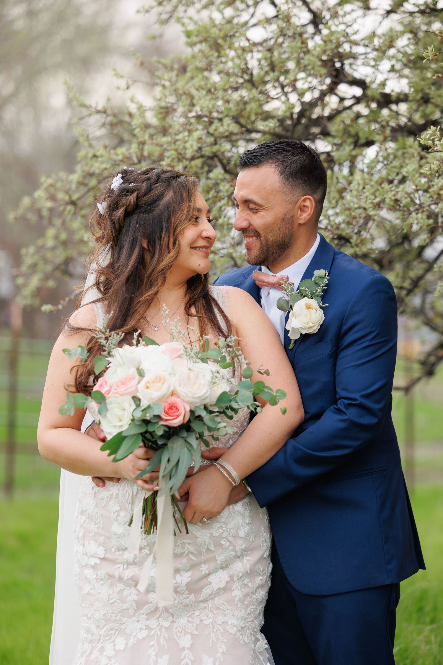 A romantic moment between newlyweds in an orchard with white and pink flowers and a navy suit.