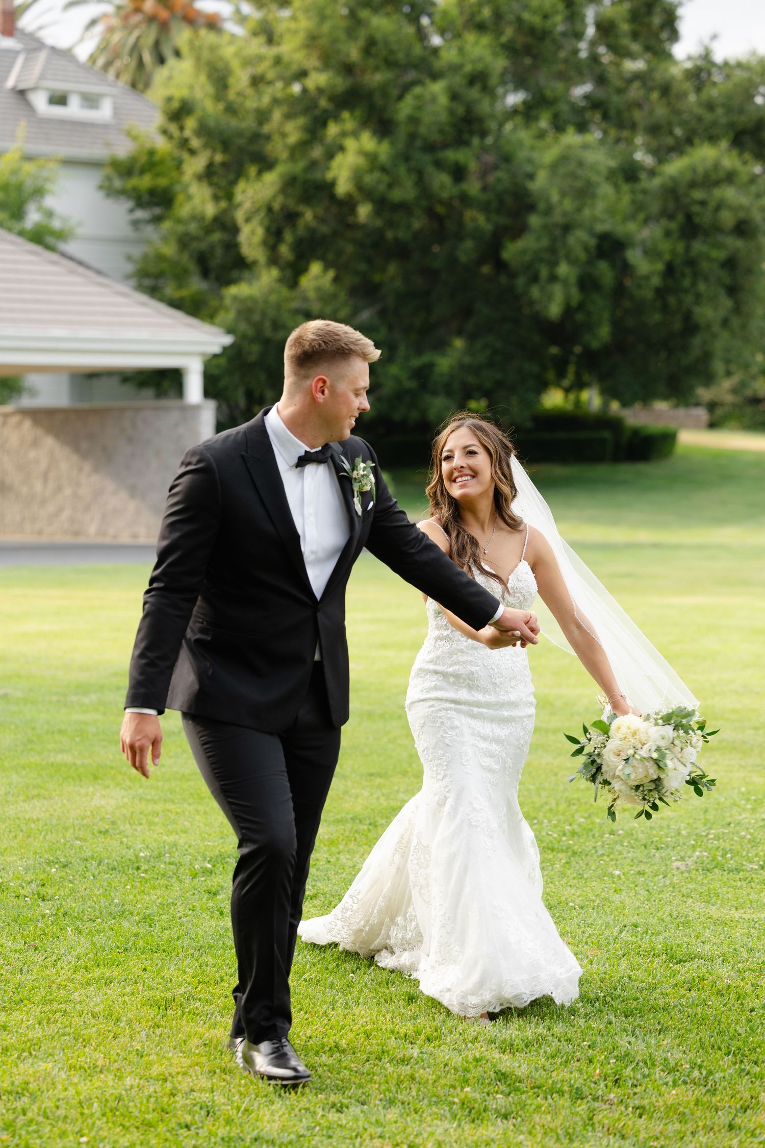 A couple in wedding attire playfully dances together on a green lawn during their special day.