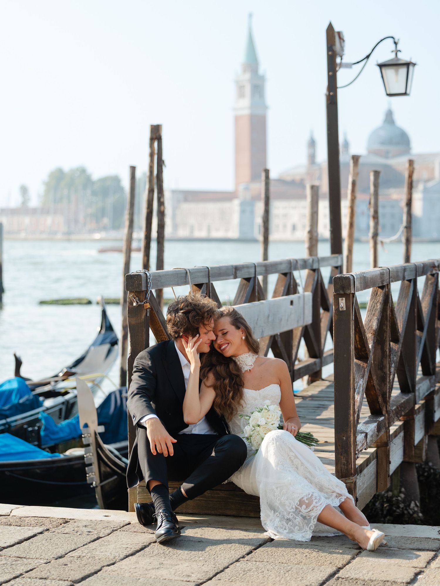Romantic couple sits on a dock in Venice with gondolas and San Giorgio Maggiore church in the background.