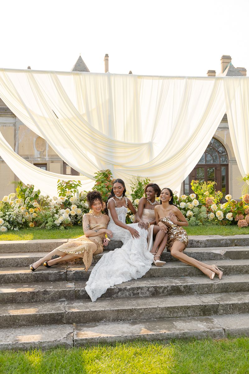 Wedding party lounging on stone steps with white drapes and floral decorations.