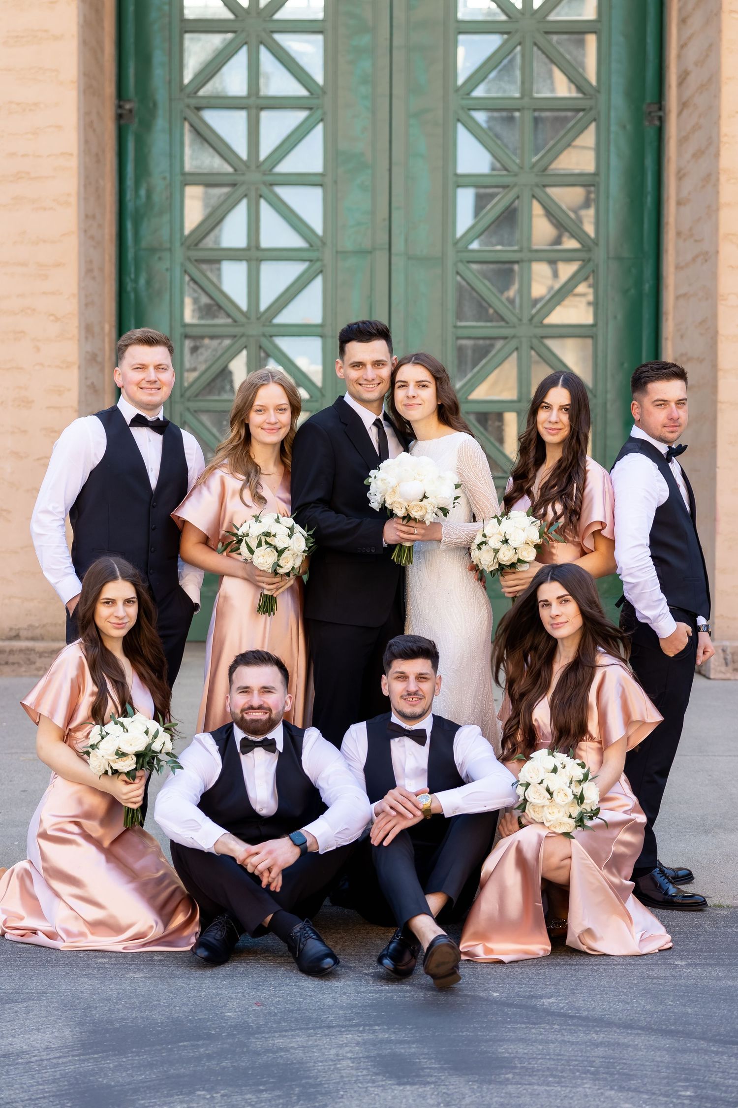 Wedding party in black and blush pink attire posed casually against a classic architectural backdrop.